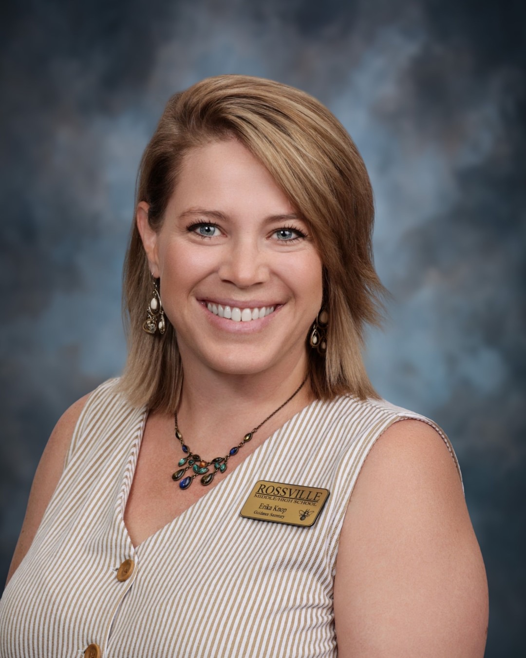 A woman with blonde hair smiles at the camera, wearing a striped vest.