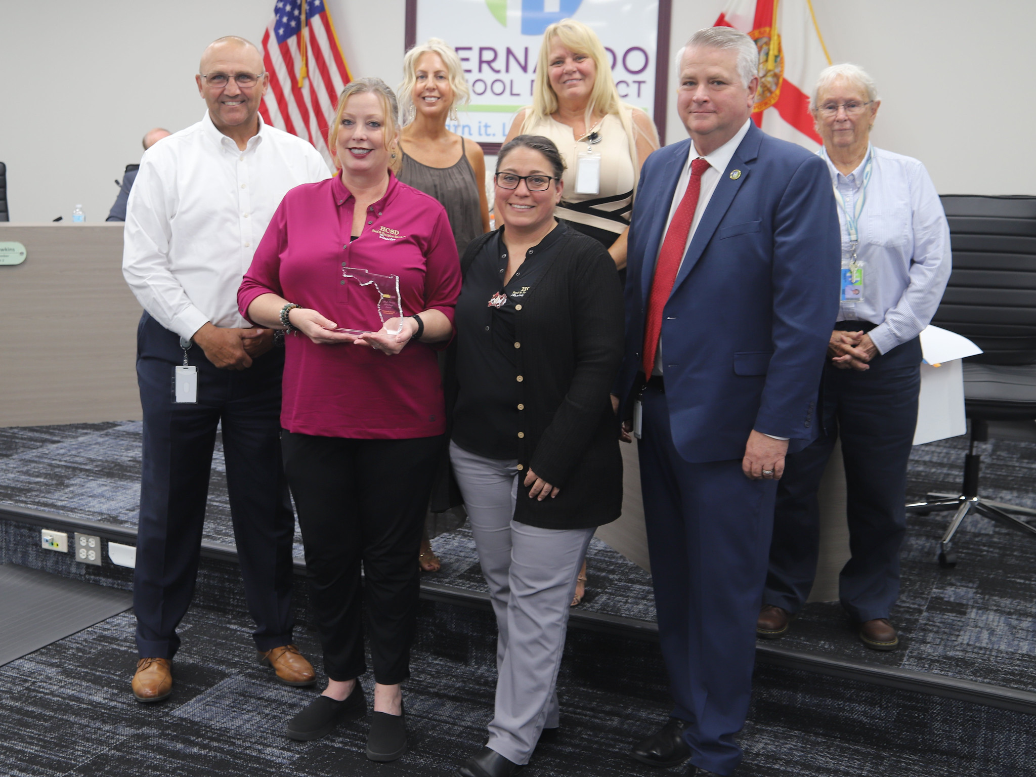 A group of people stand together, with one woman holding a small award.