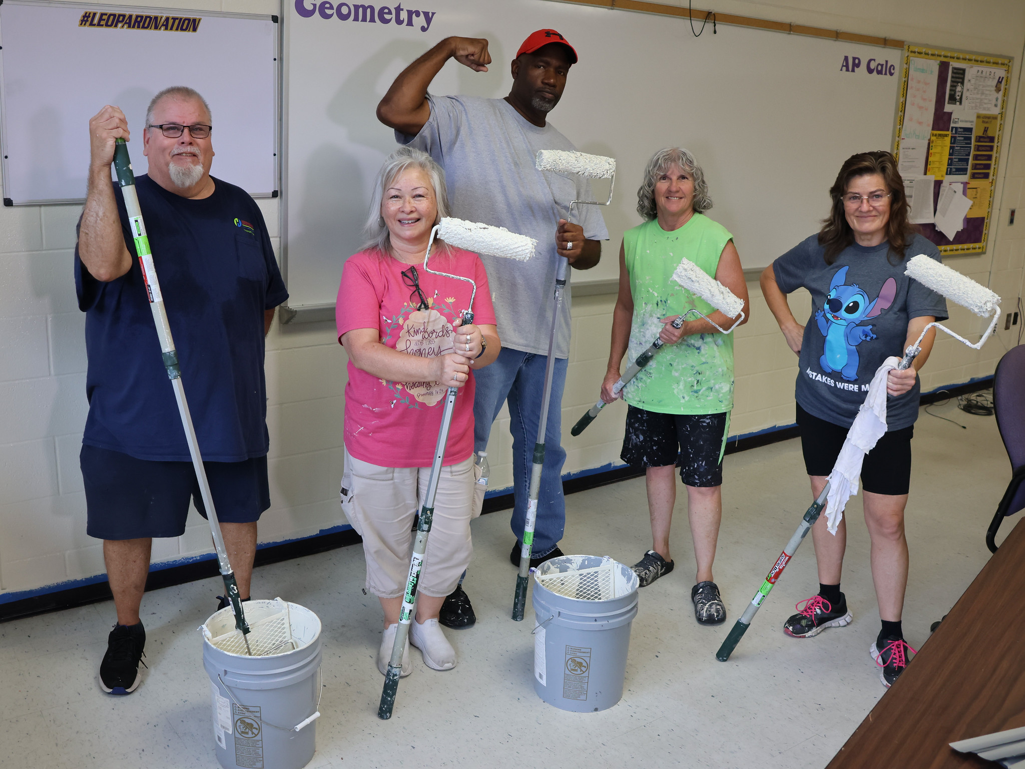 Five people stand in a room, each holding a paint roller and bucket, ready to paint.