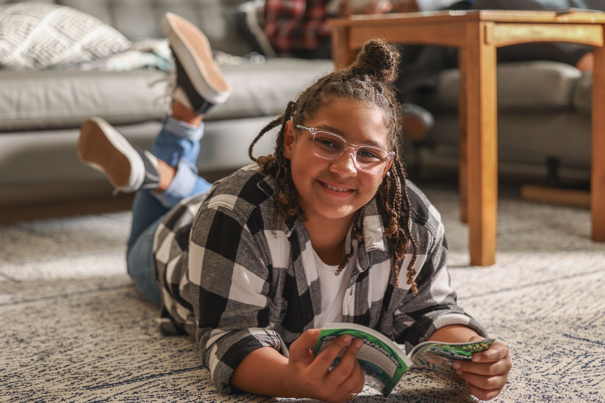 A young person with glasses and hair in a bun lies on a carpeted floor, holding money.