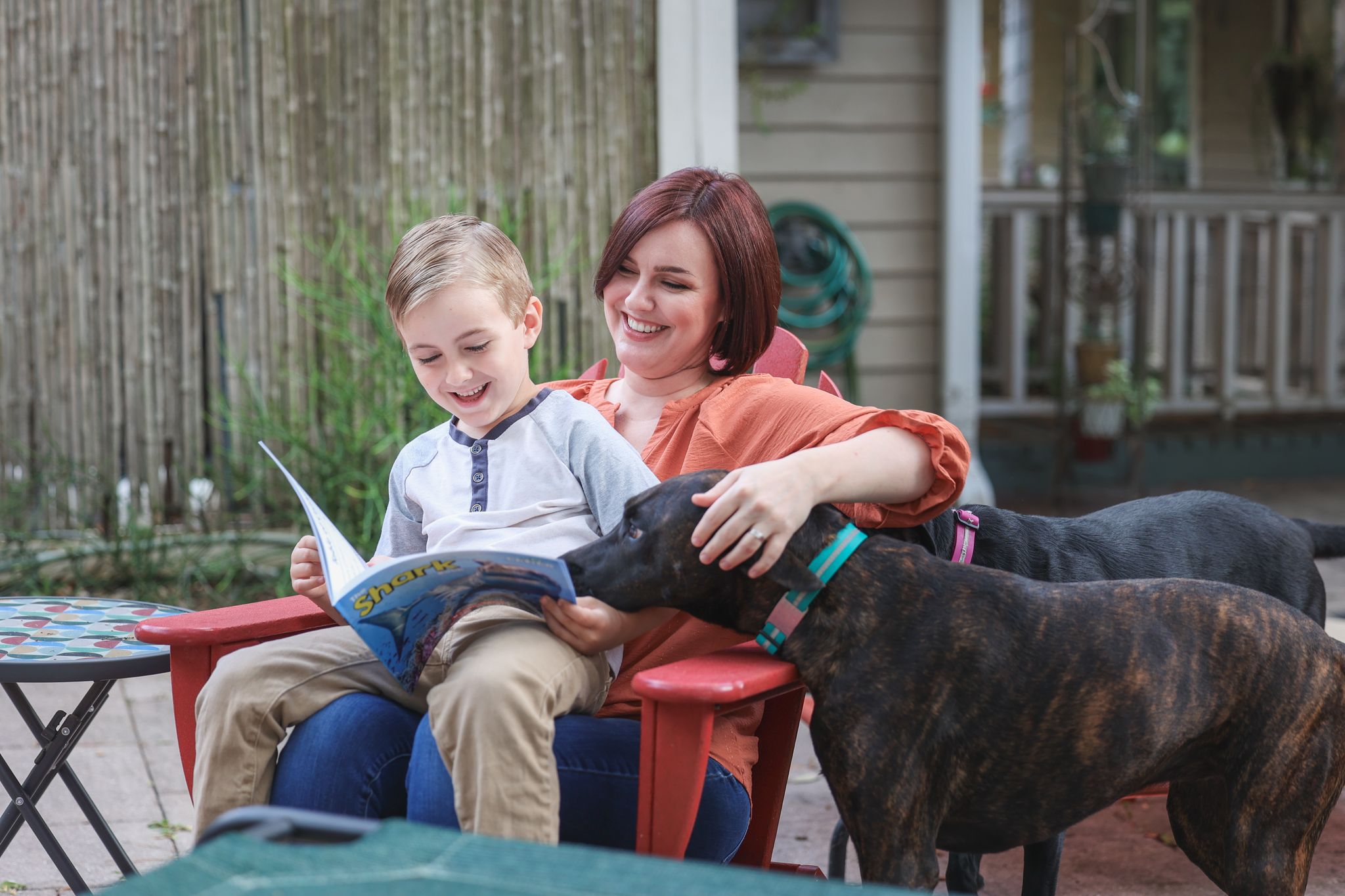 A woman and a young boy sit outdoors, with two dogs nearby.
