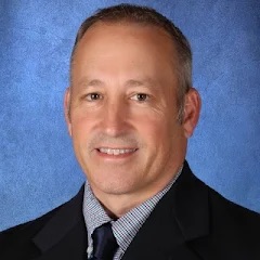 A man with short, graying hair smiles at the camera.
