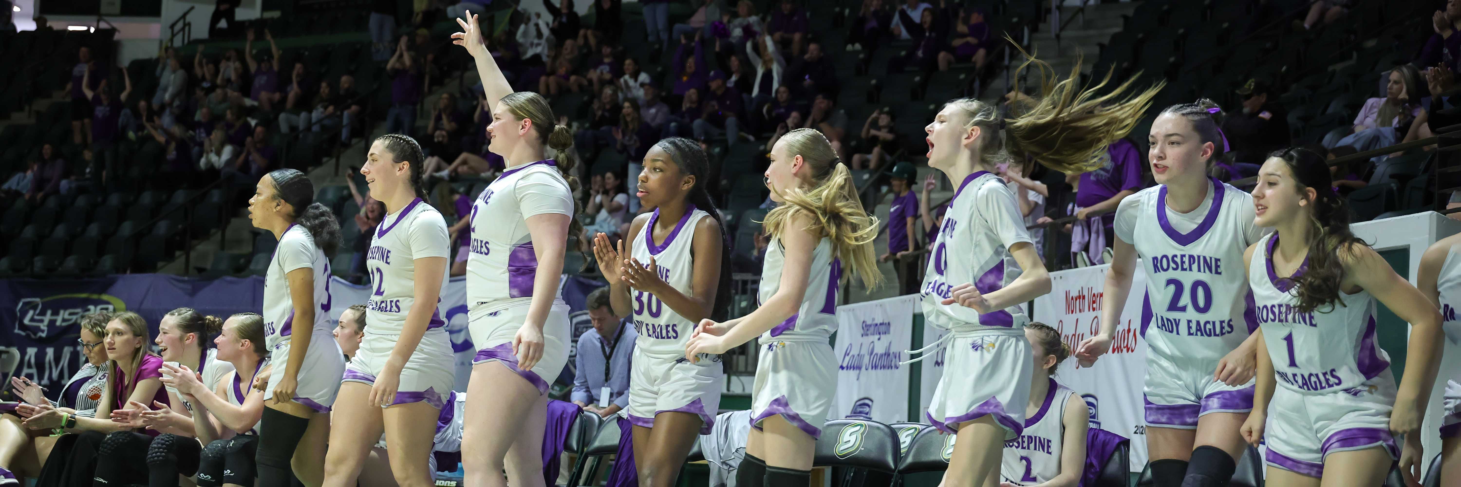 A basketball team stands together on the court, celebrating.