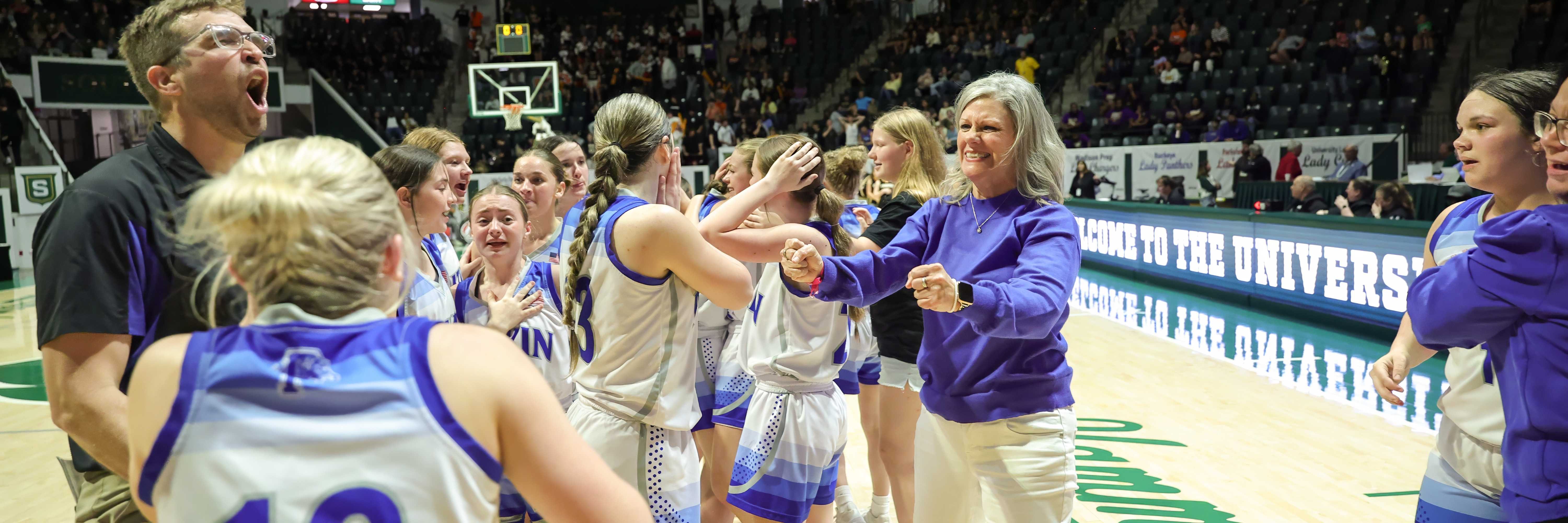 A basketball team celebrates on the court, high-fiving and cheering.
