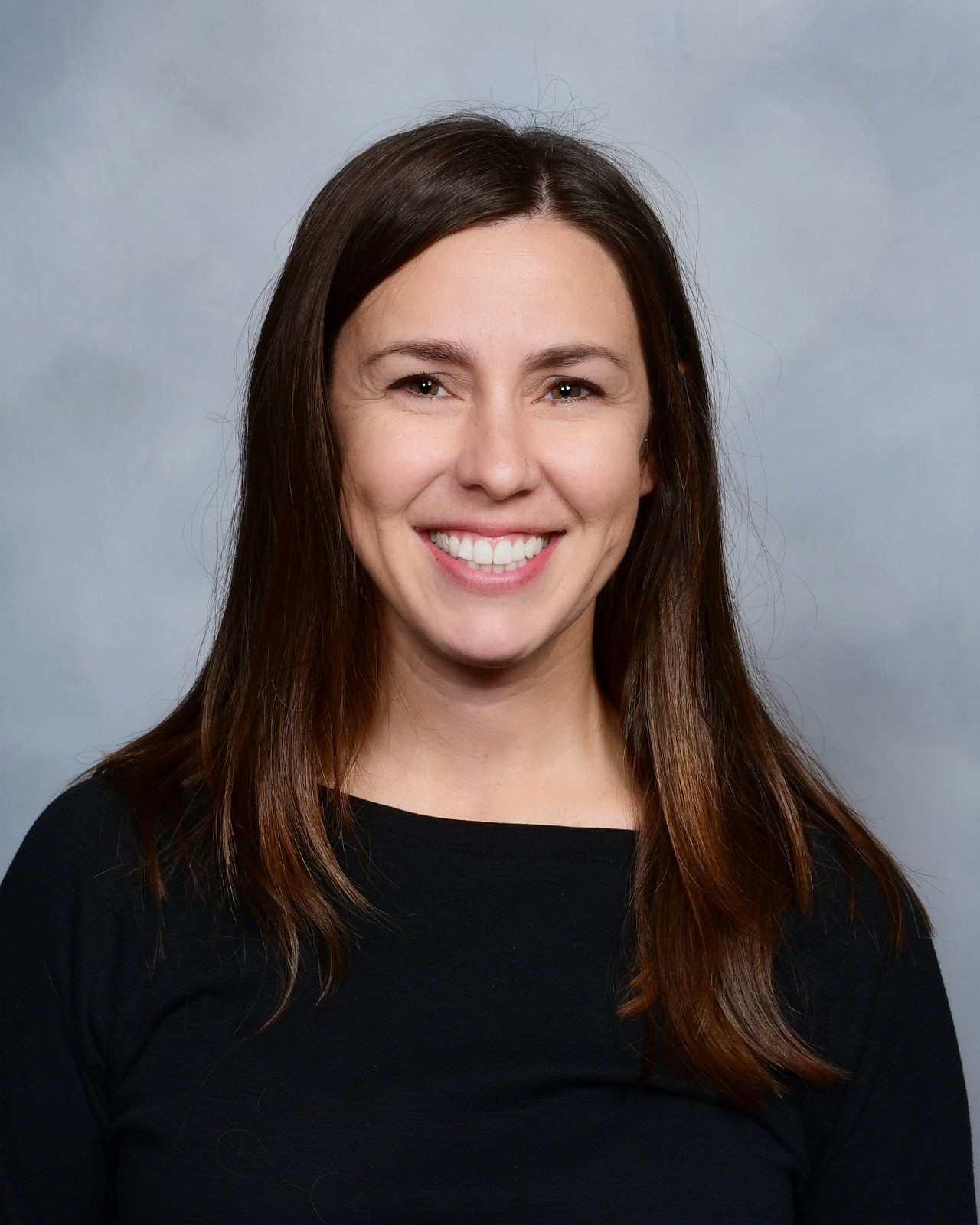 A woman with long brown hair smiles at the camera.
