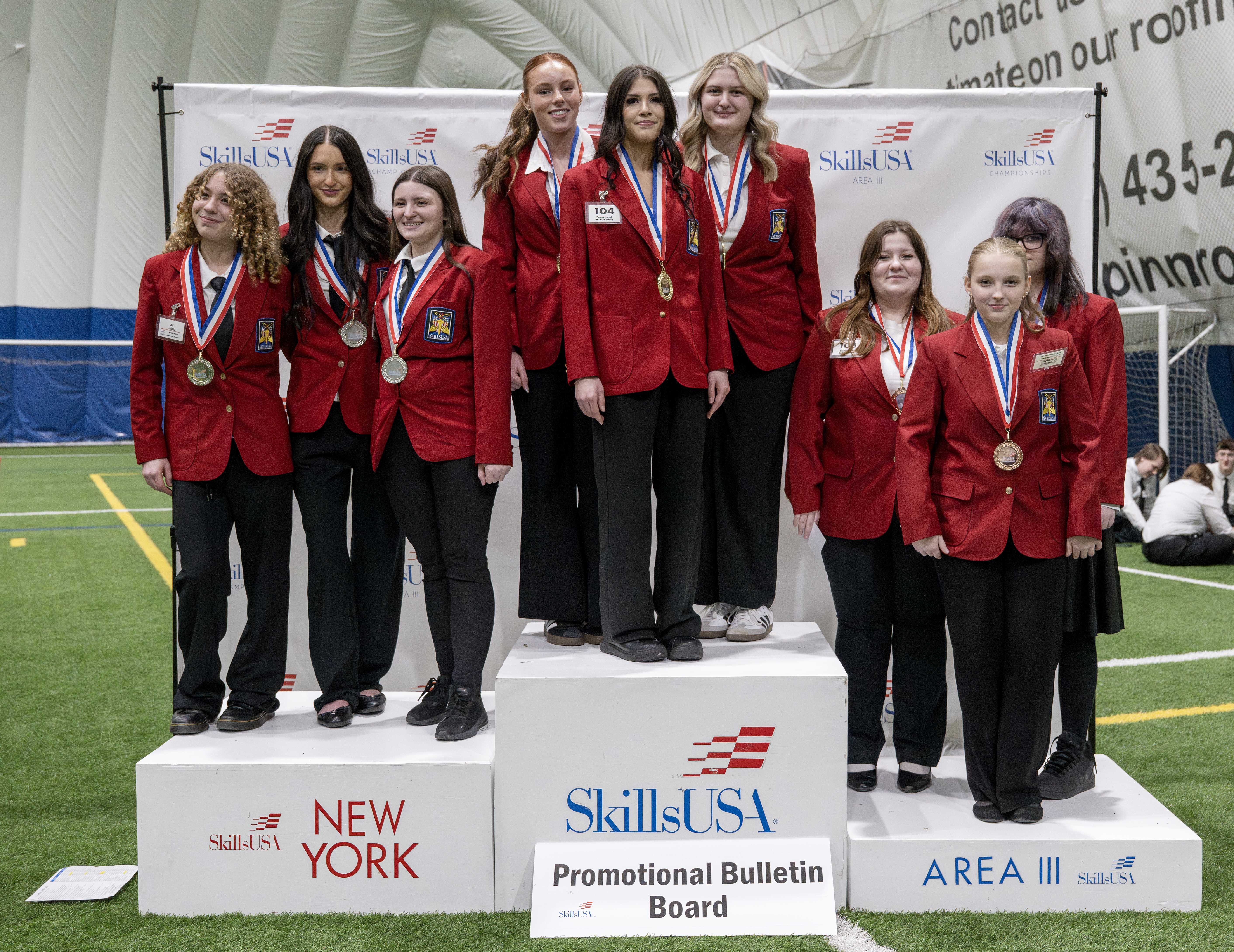 A group of young people in red blazers stand on a podium, wearing medals.