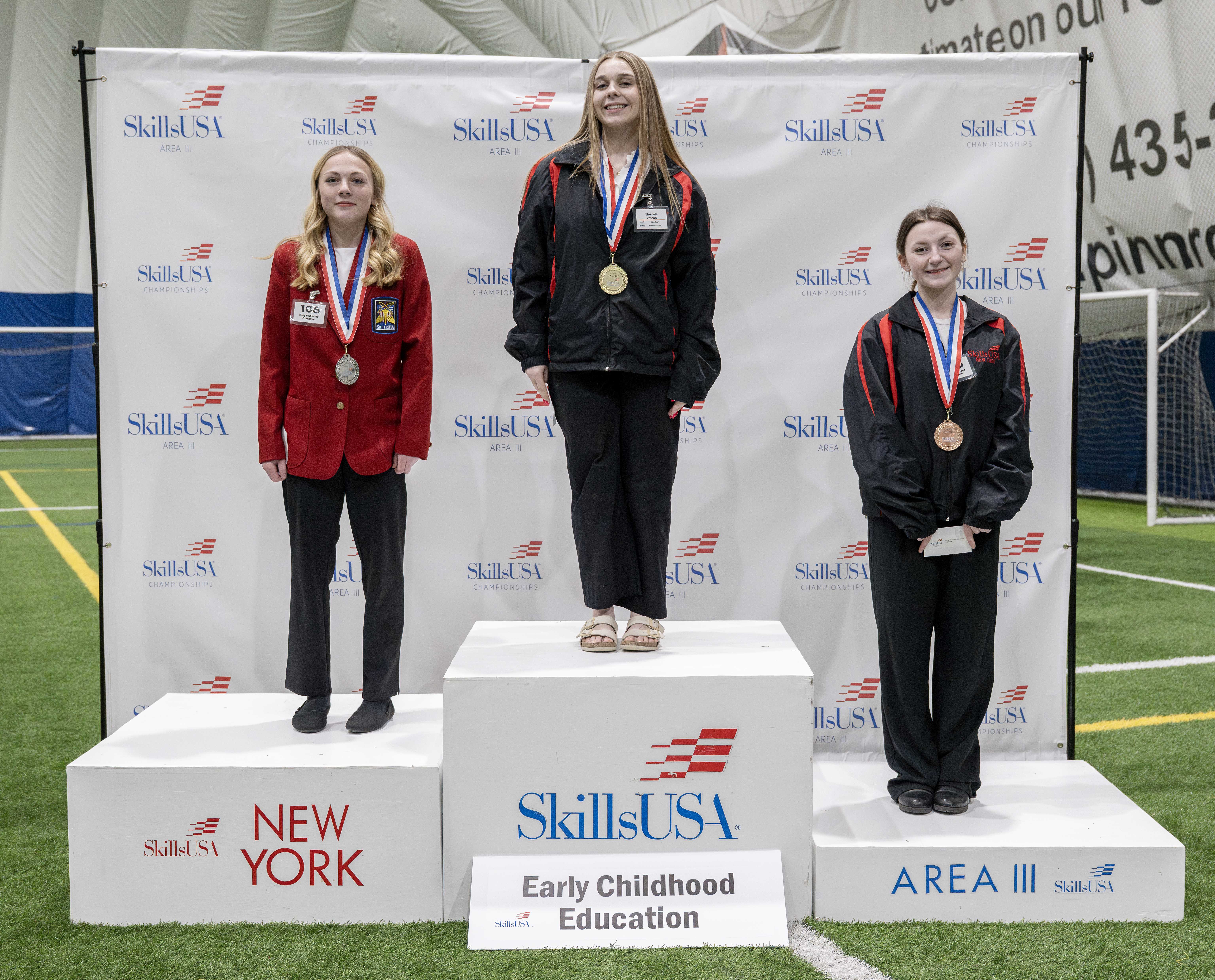 Three people stand on a podium, each wearing a medal.