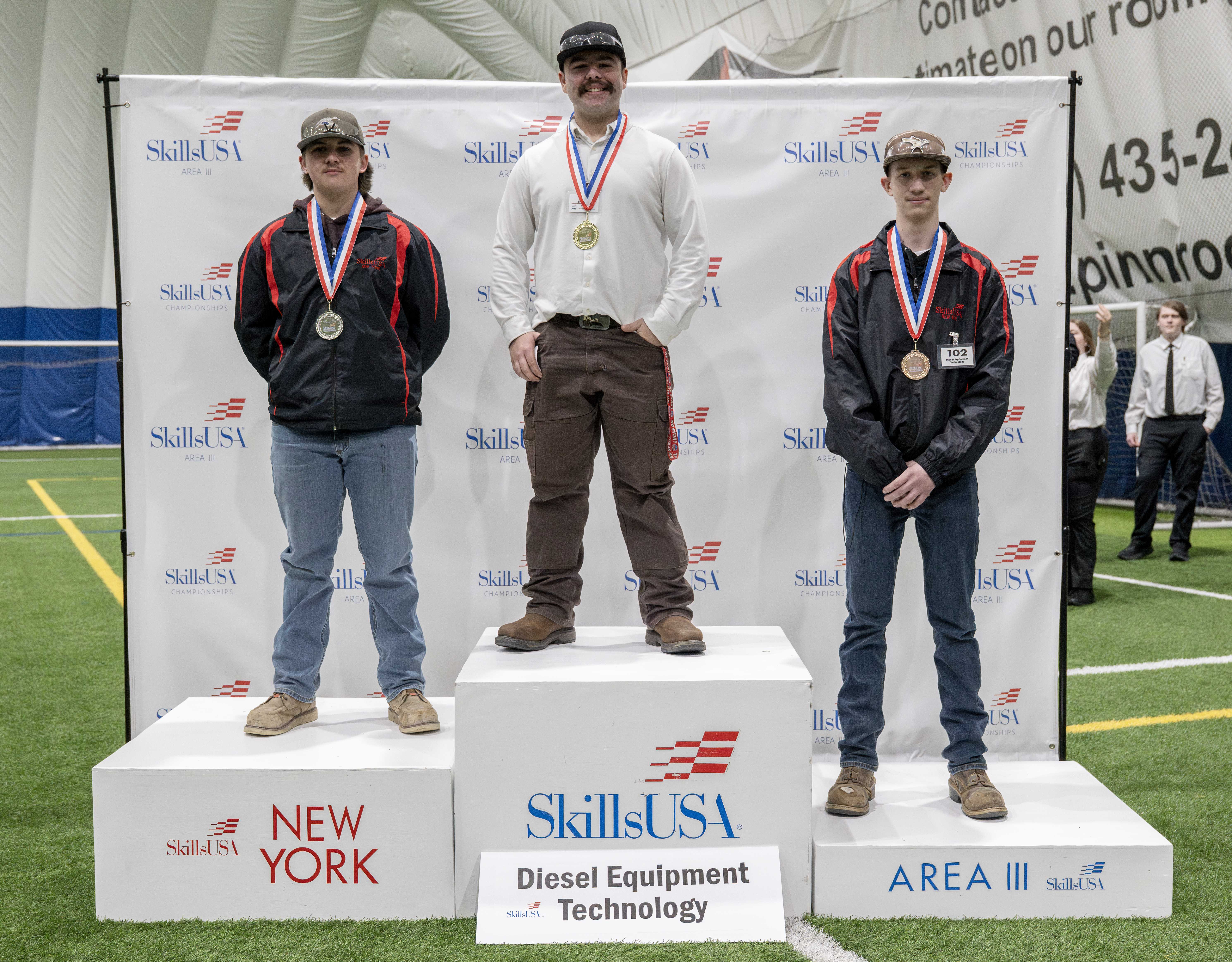Three young men stand on a podium, each wearing a medal.