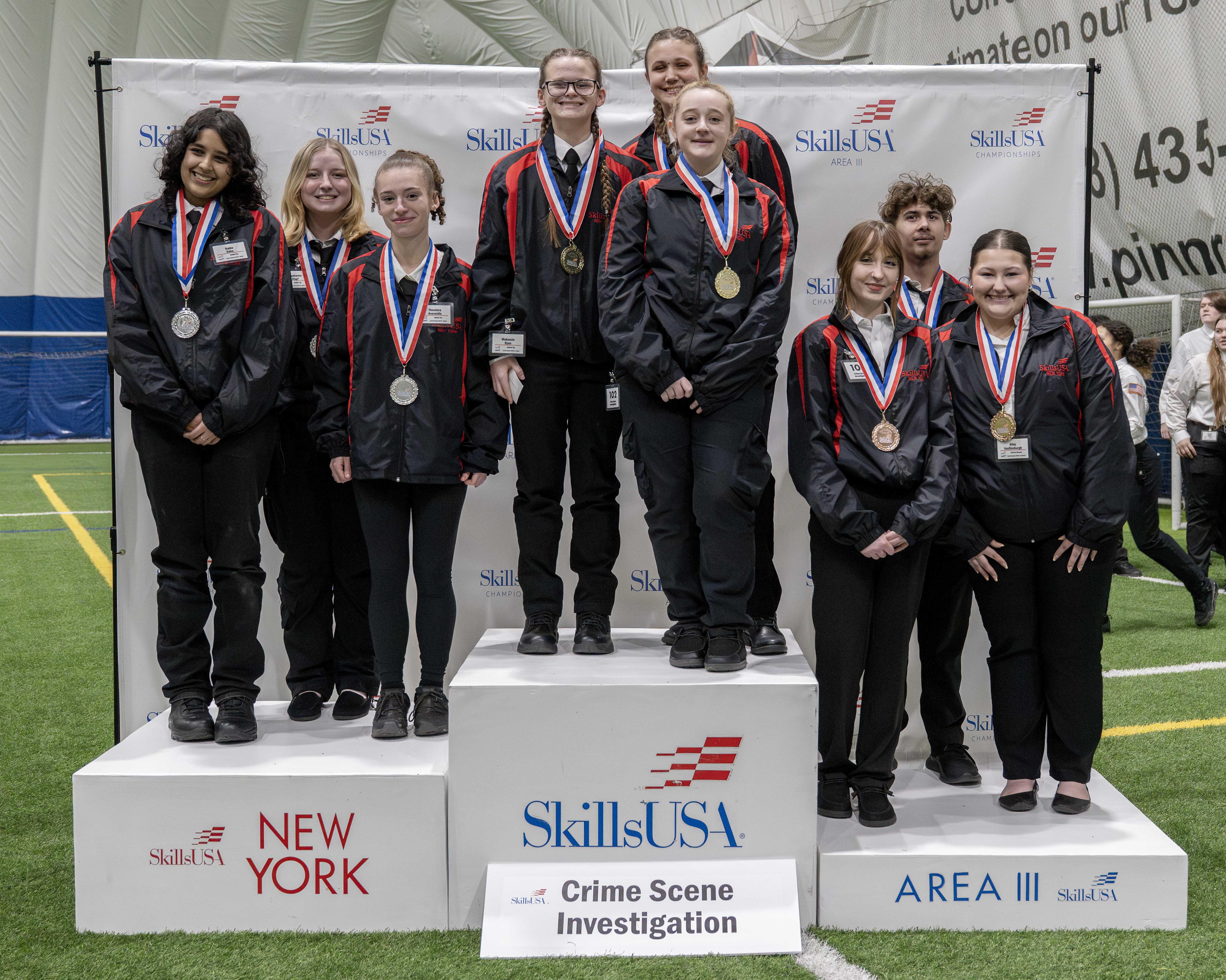 A group of people stand on a podium, wearing medals and jackets.