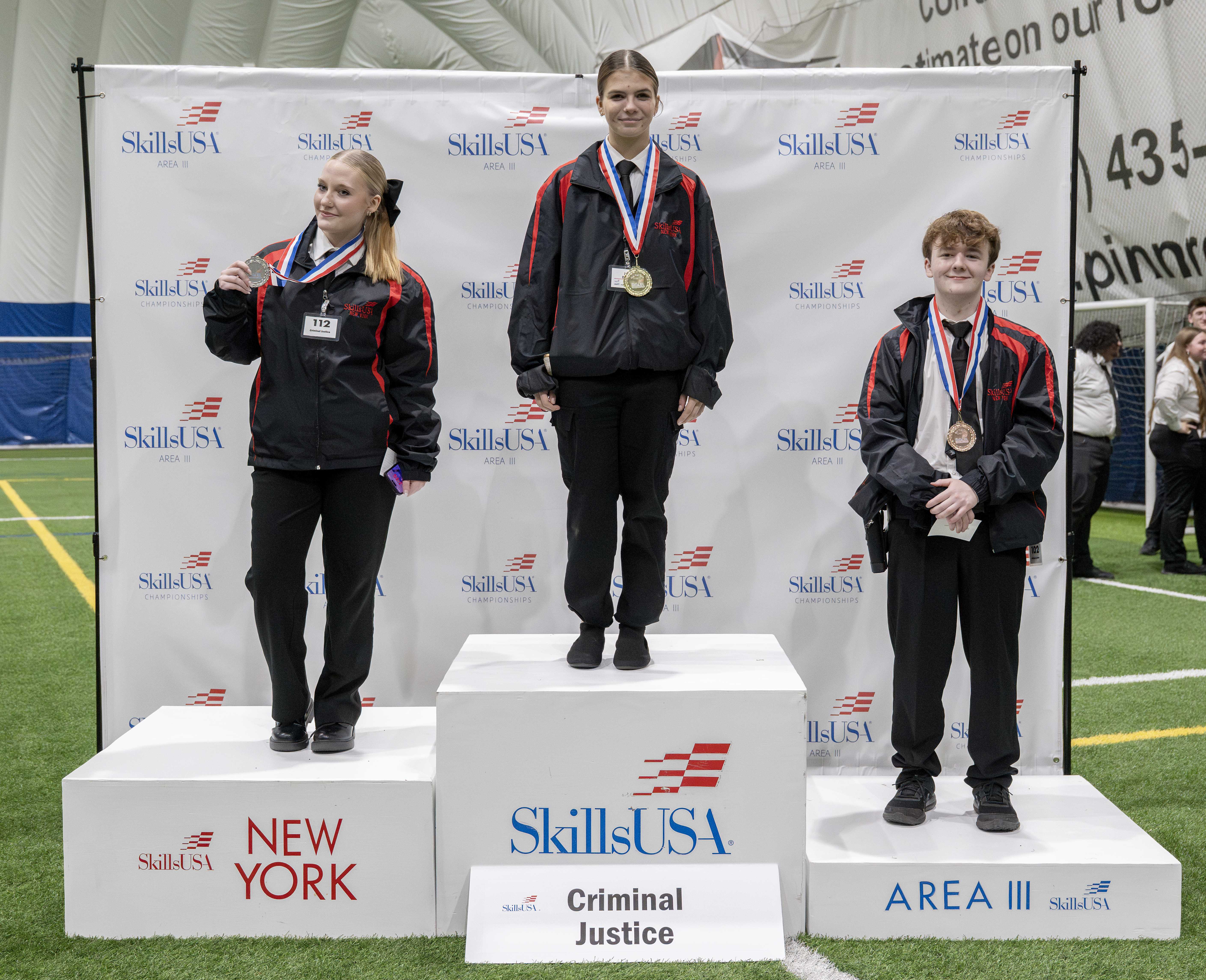 Three young people stand on a podium, each wearing a medal, celebrating a competition.