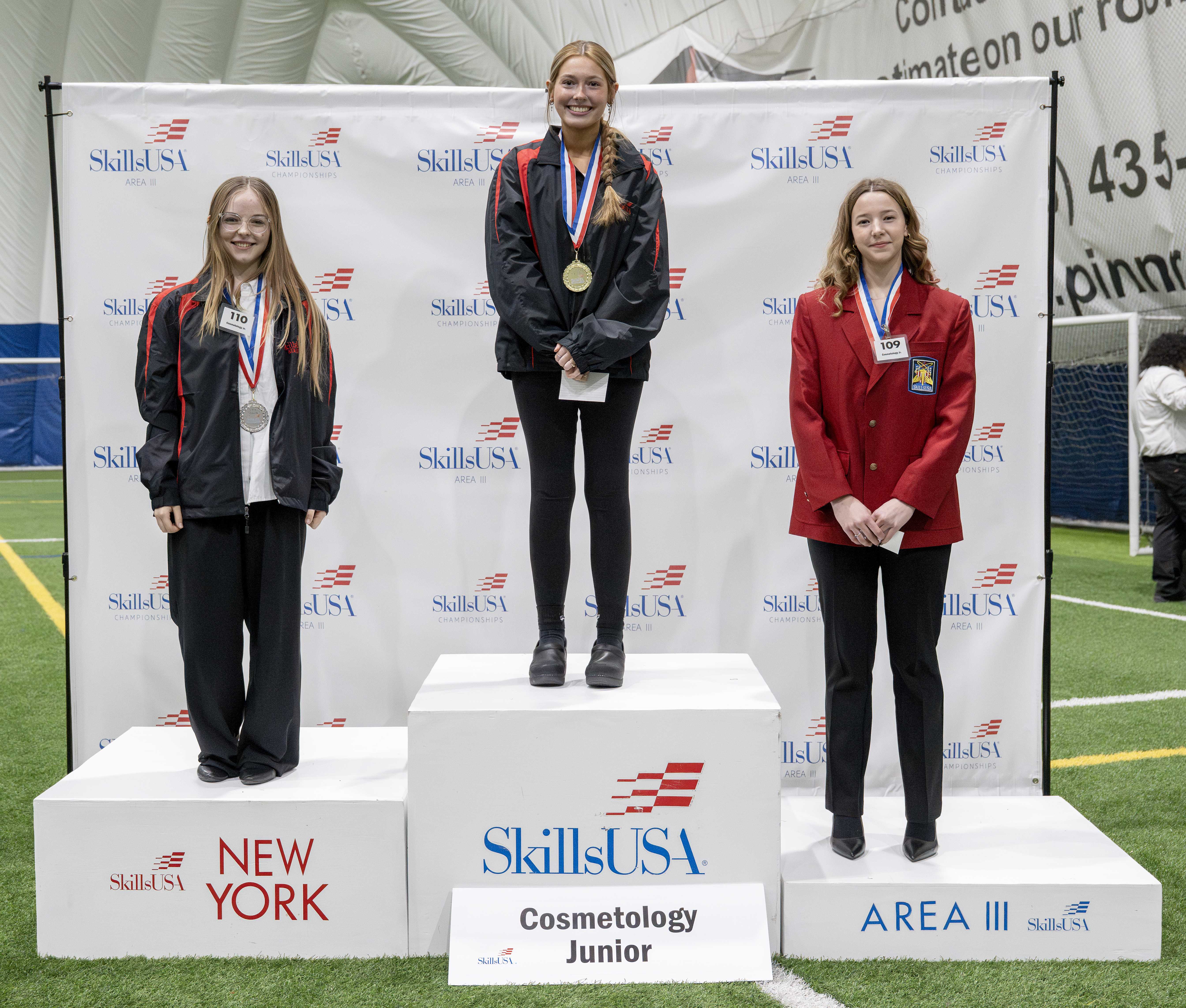 Three young women stand on a podium, each wearing a medal.