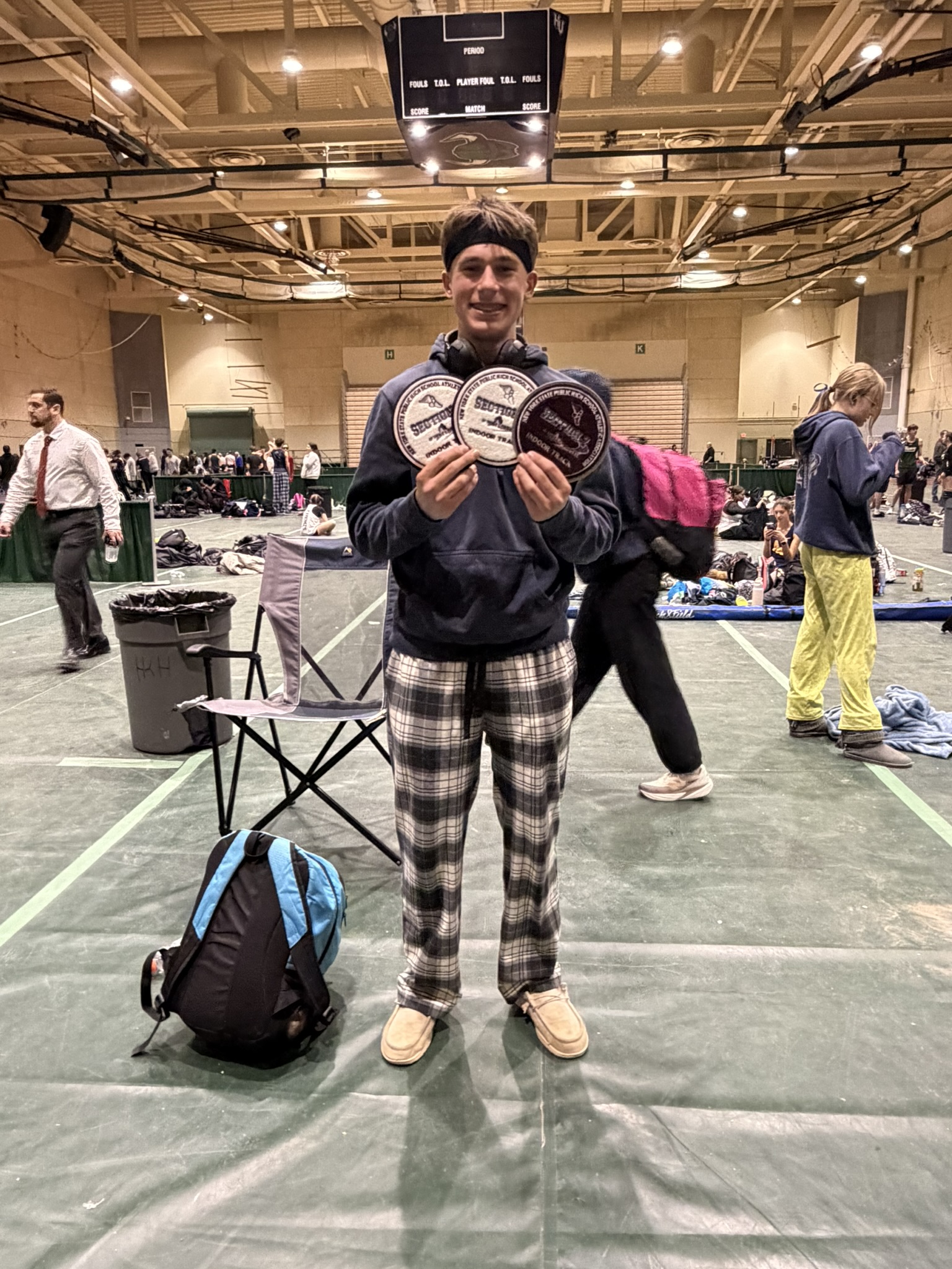 A young athlete proudly displays three awards in a gymnasium.