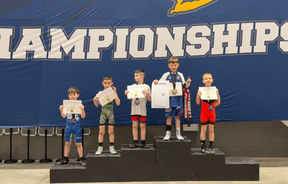 Young wrestlers stand on a podium, holding certificates and medals, with Dawson on the top pedestal.