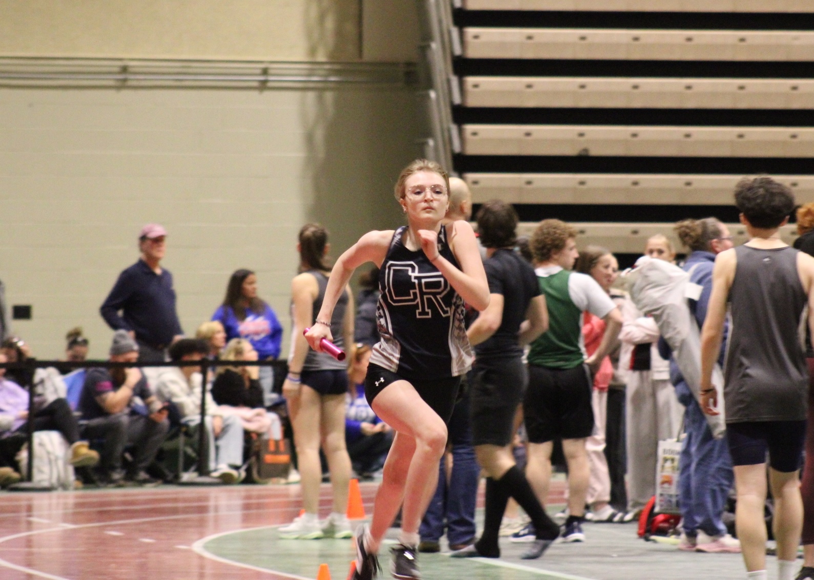 A young woman runs in a track and field relay race, holding a baton.
