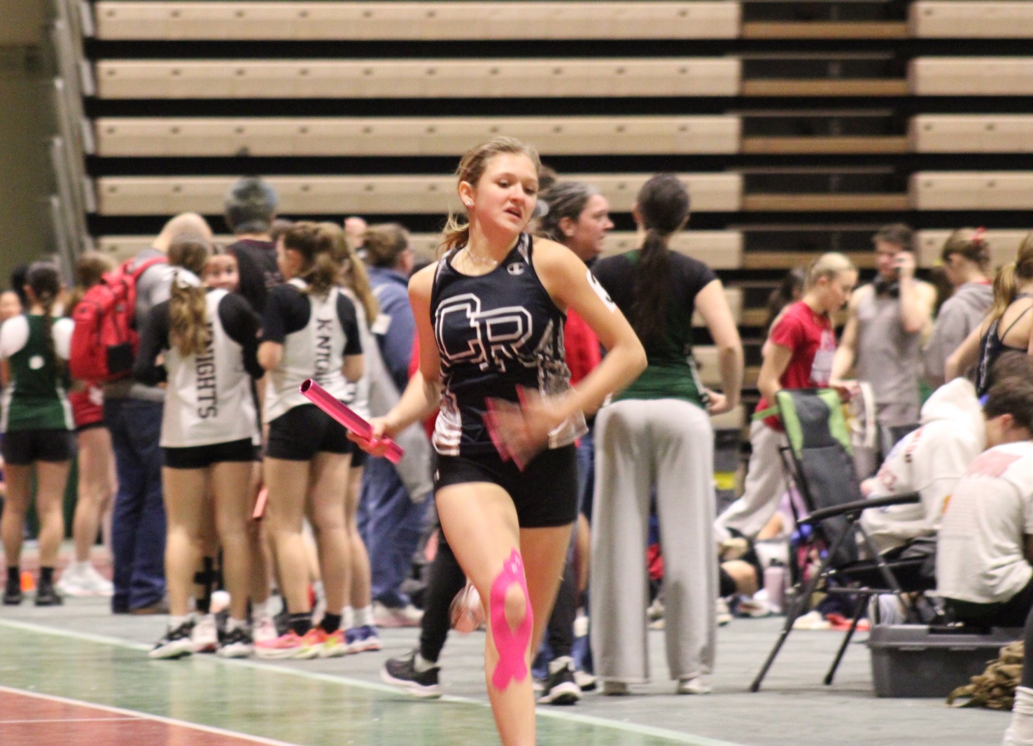 A young woman in athletic wear runs with a baton during a track event.