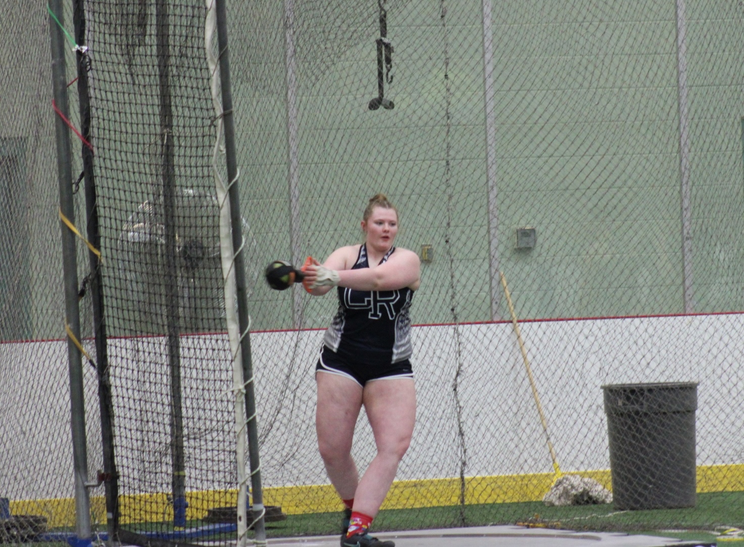 A female athlete prepares to throw a hammer in an indoor track and field setting.
