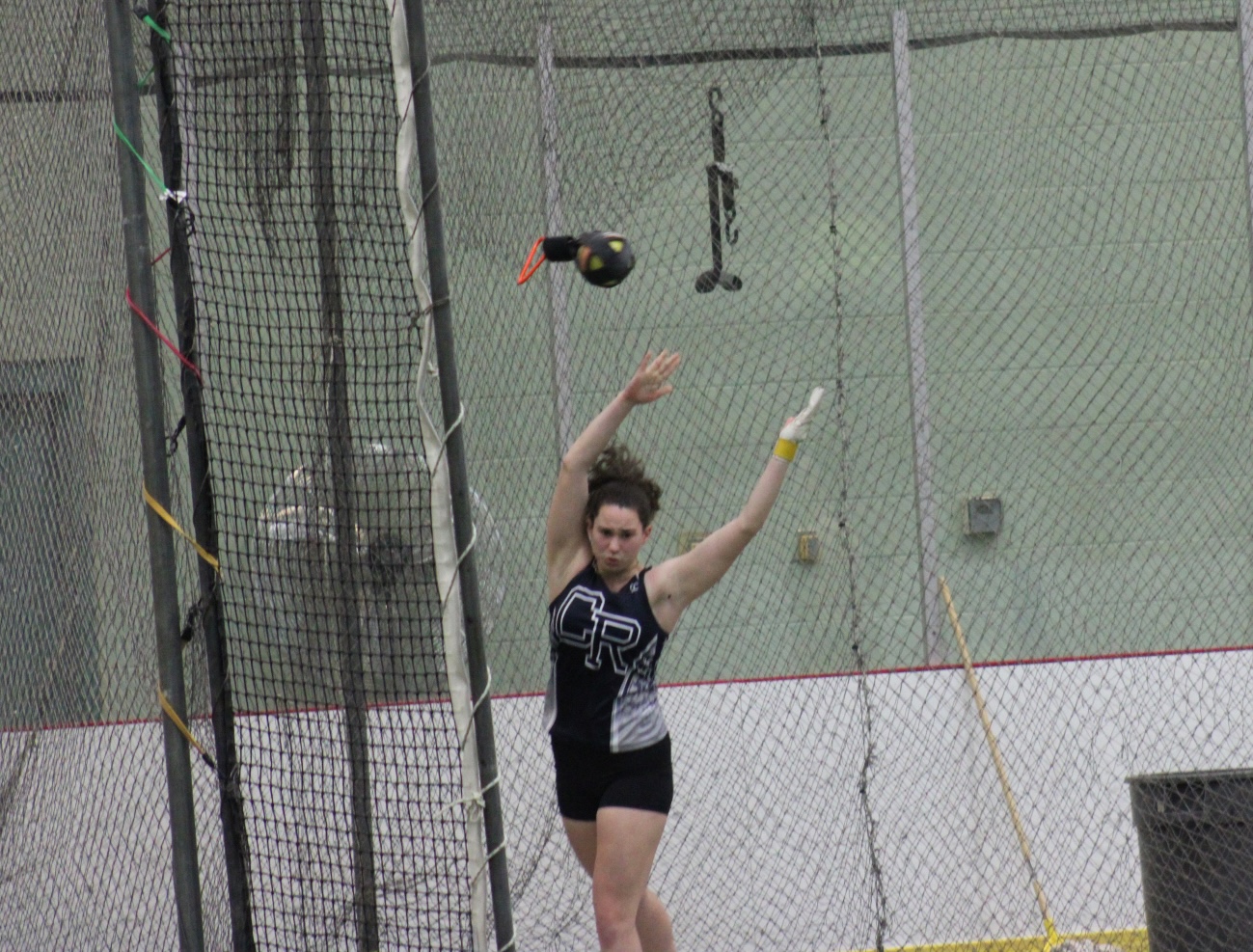 A female athlete throws a hammer in an indoor track and field setting.