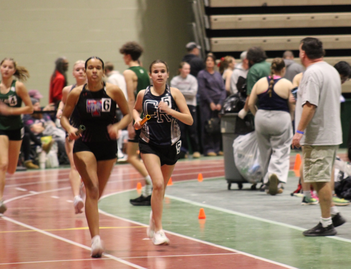 Runners compete in an indoor track and field event, sprinting down the track.