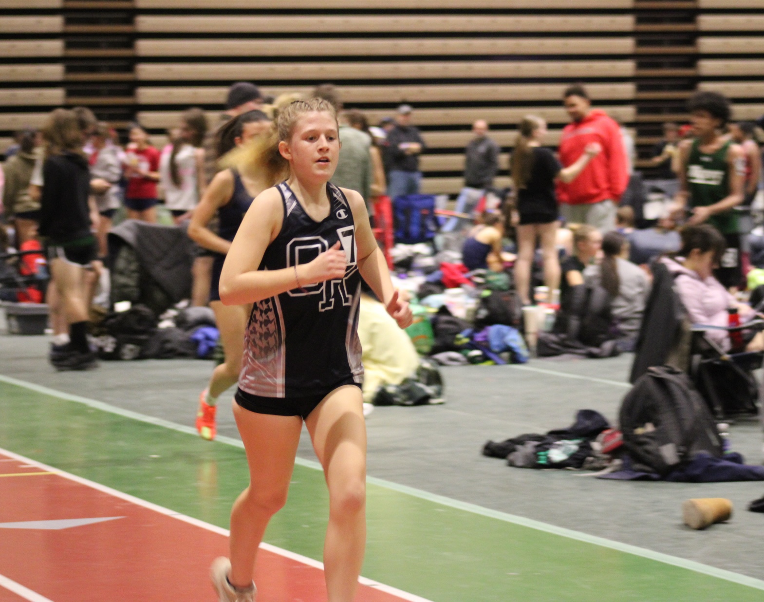 A young woman runs on an indoor track during a competition.
