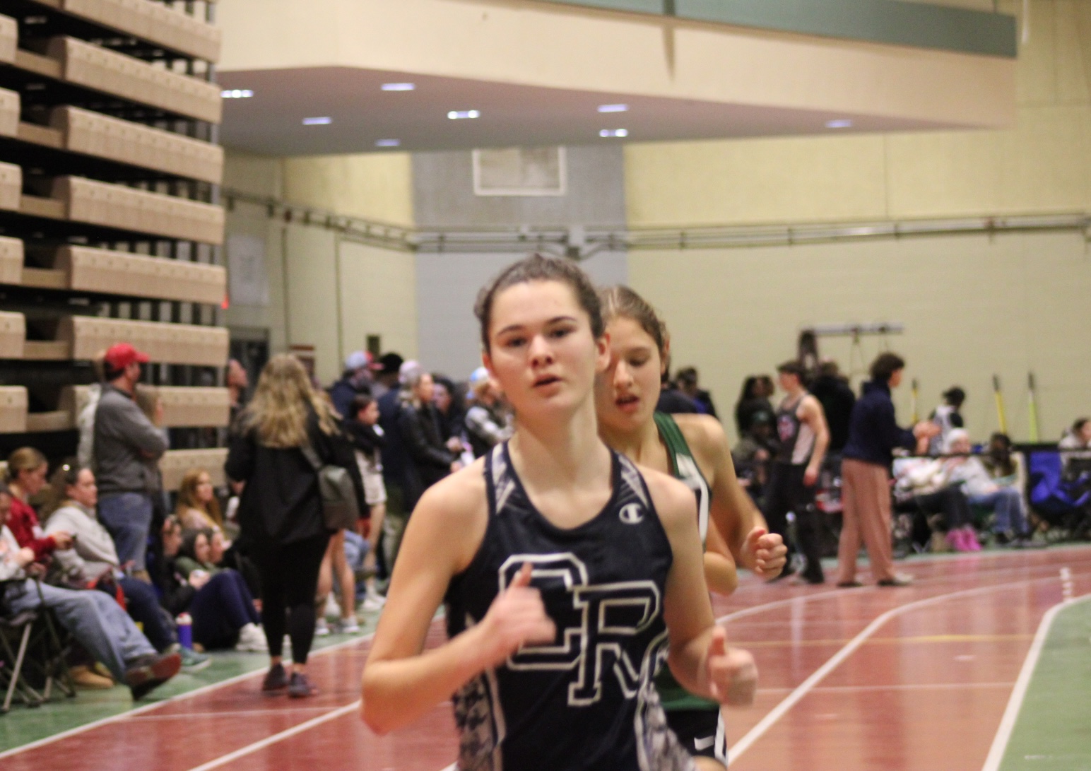 A female athlete run on an indoor track during a competition.