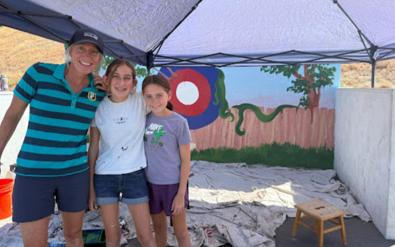 Students and teacher pose in front of a painted mural under a canopy.