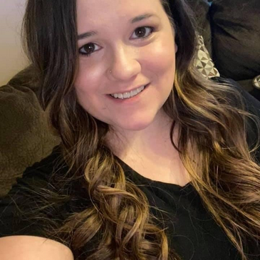 A woman with long, wavy brown hair smiles at the camera.