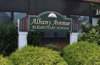 A sign for Albany Avenue Elementary School stands in front of a building.