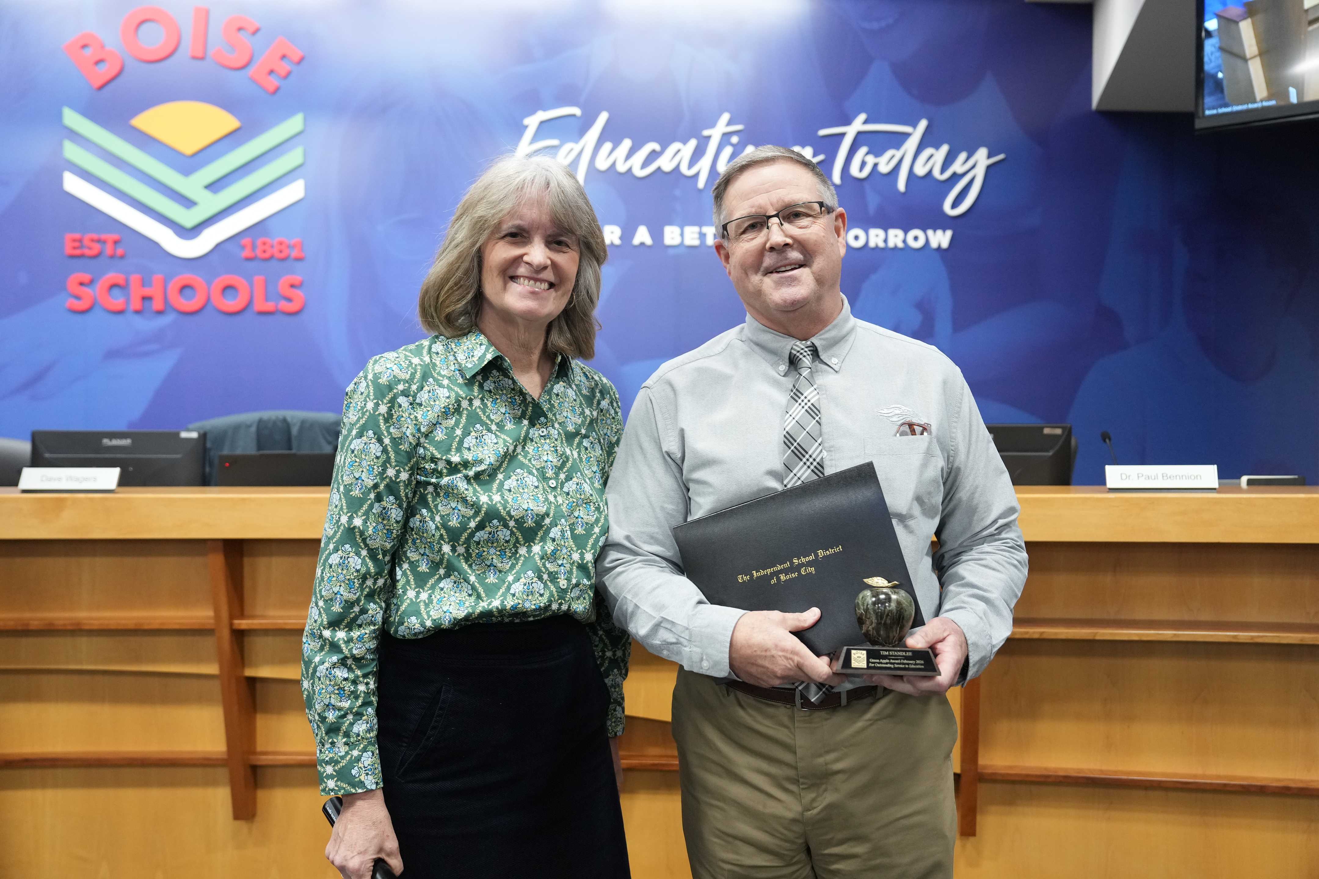 Two people stand together, smiling, in front of a Boise Schools backdrop.