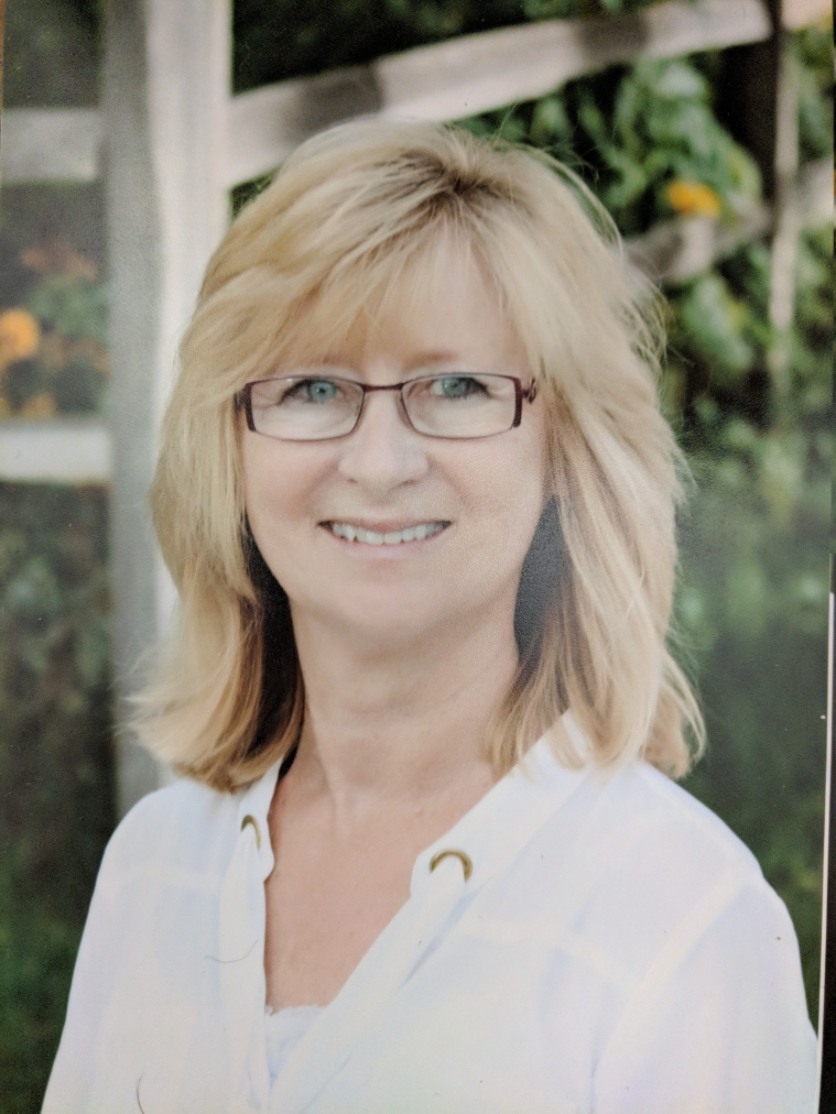 A woman with blonde hair and glasses smiles at the camera.