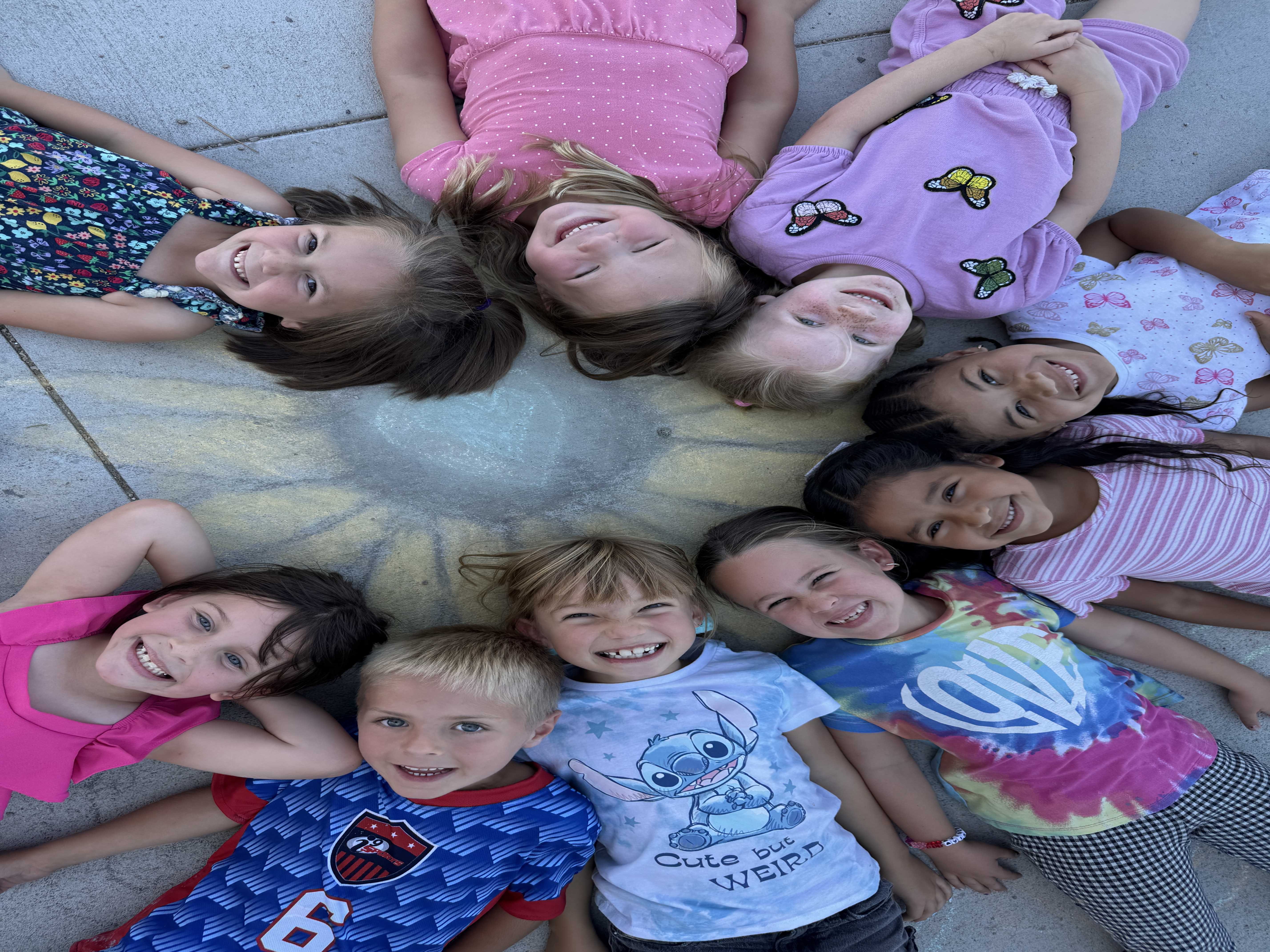 A group of diverse children lie in a circle on the ground, smiling up at the camera.
