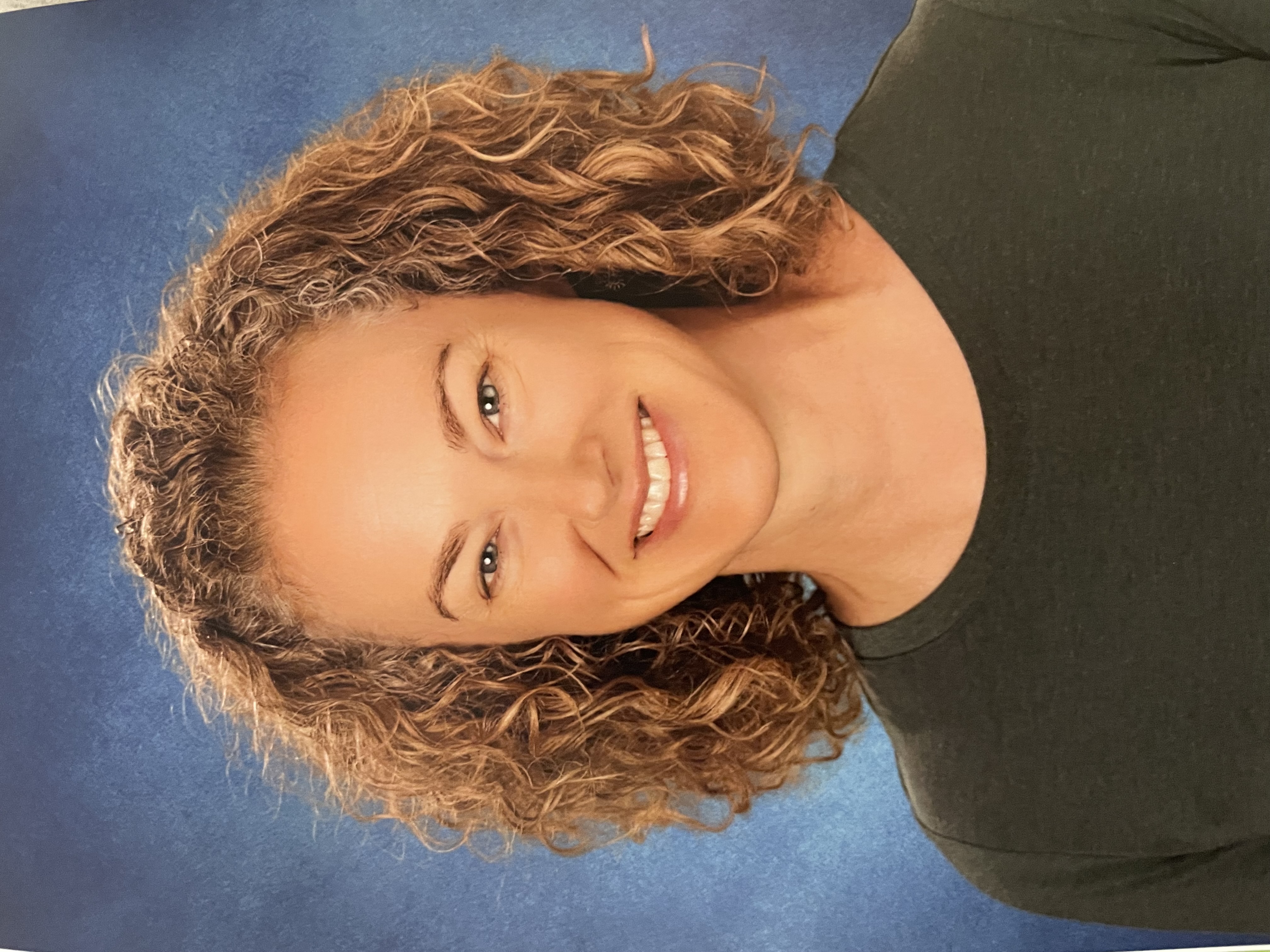 A woman with curly brown hair smiles at the camera.