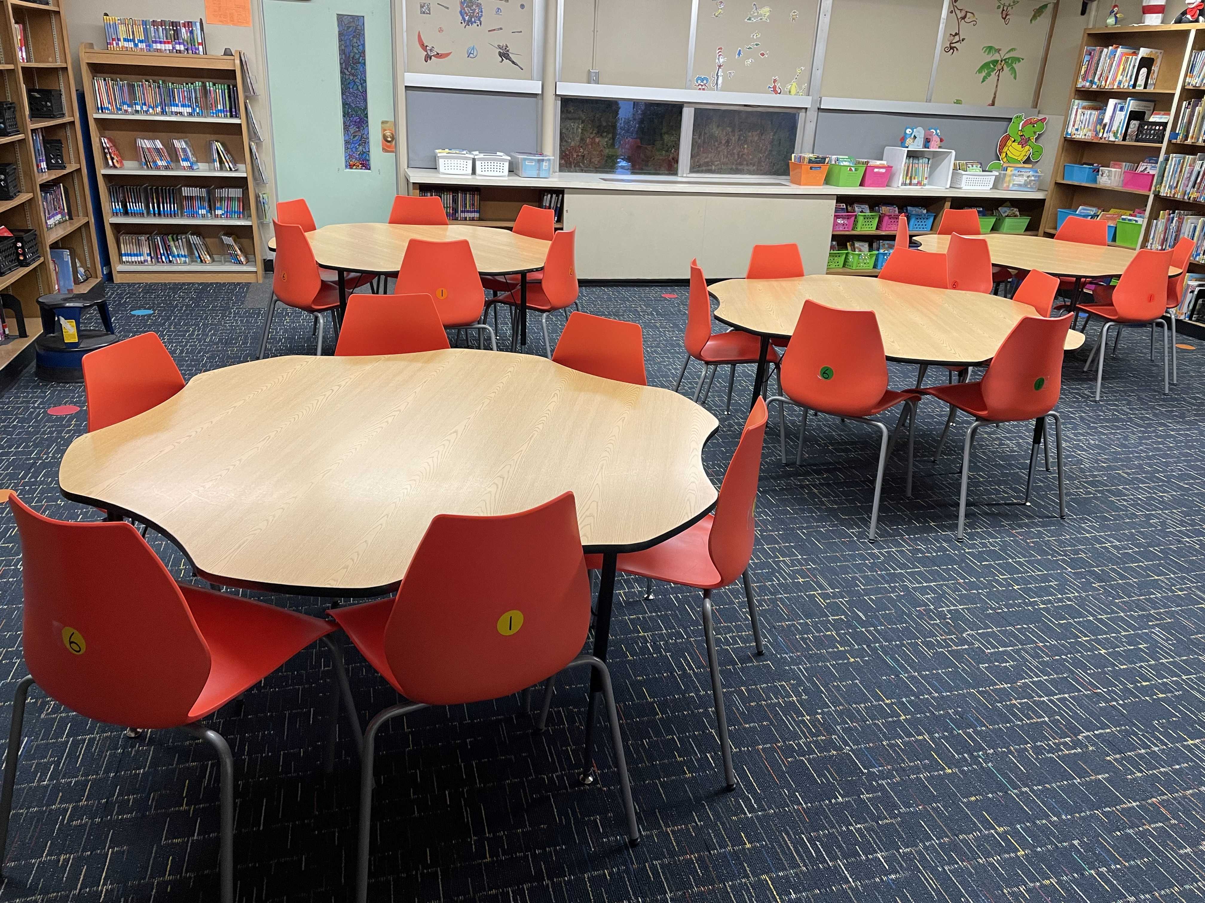 A library or classroom with round tables and red chairs, ready for students.