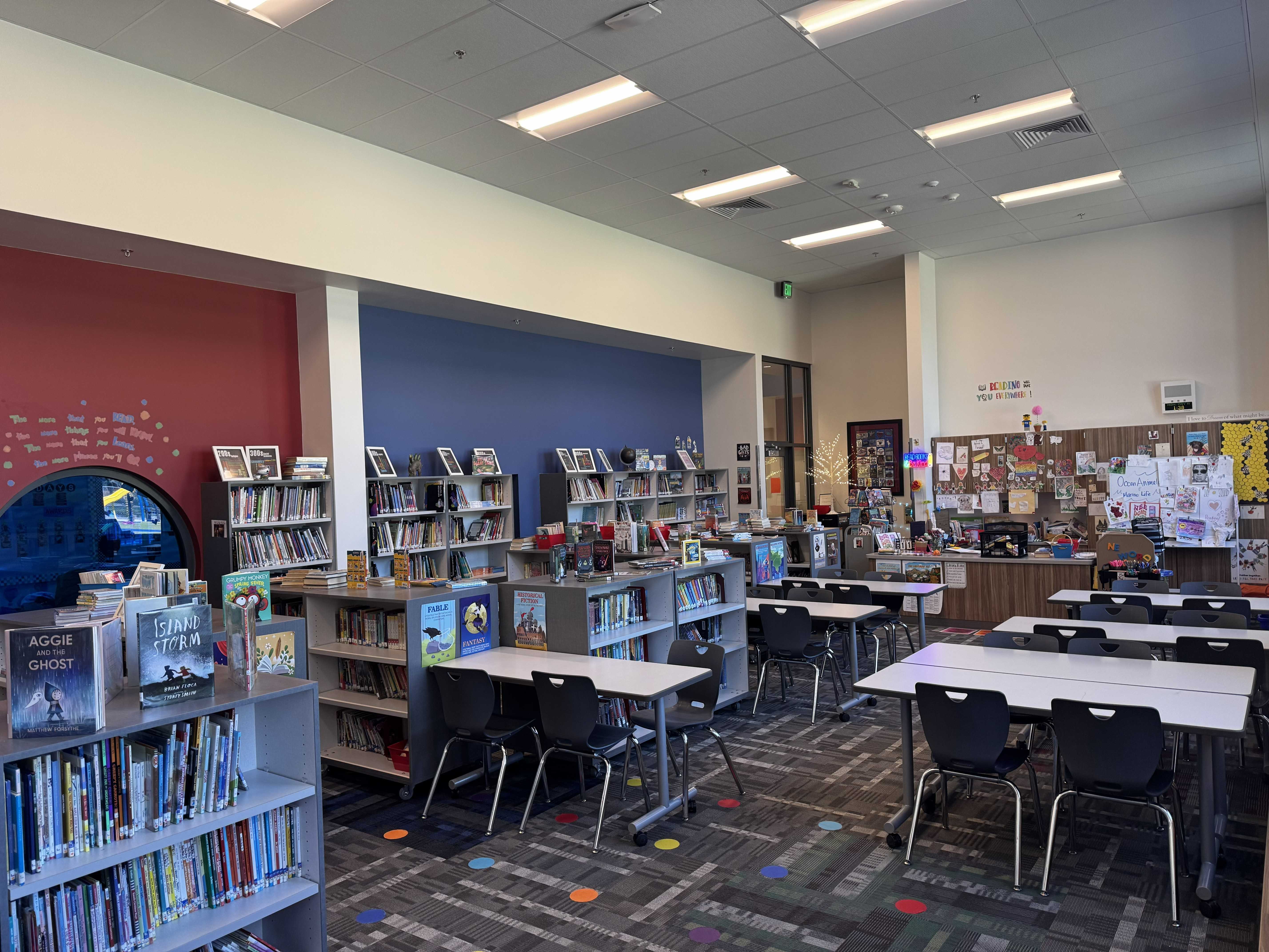 A well-lit library with bookshelves, tables, and chairs.