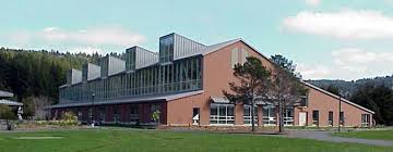 A modern brick building with a glass facade stands on a green lawn.