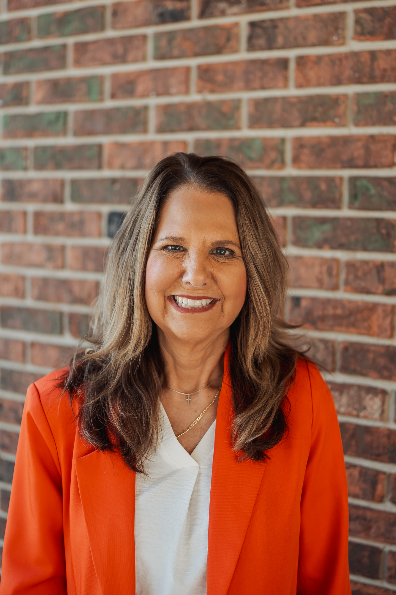 A woman with long brown hair smiles in front of a brick wall.