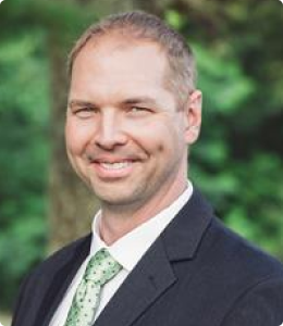 A man in a suit smiles at the camera, with a green tie.