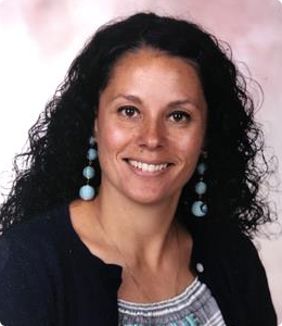 A woman with curly dark hair smiles at the camera.