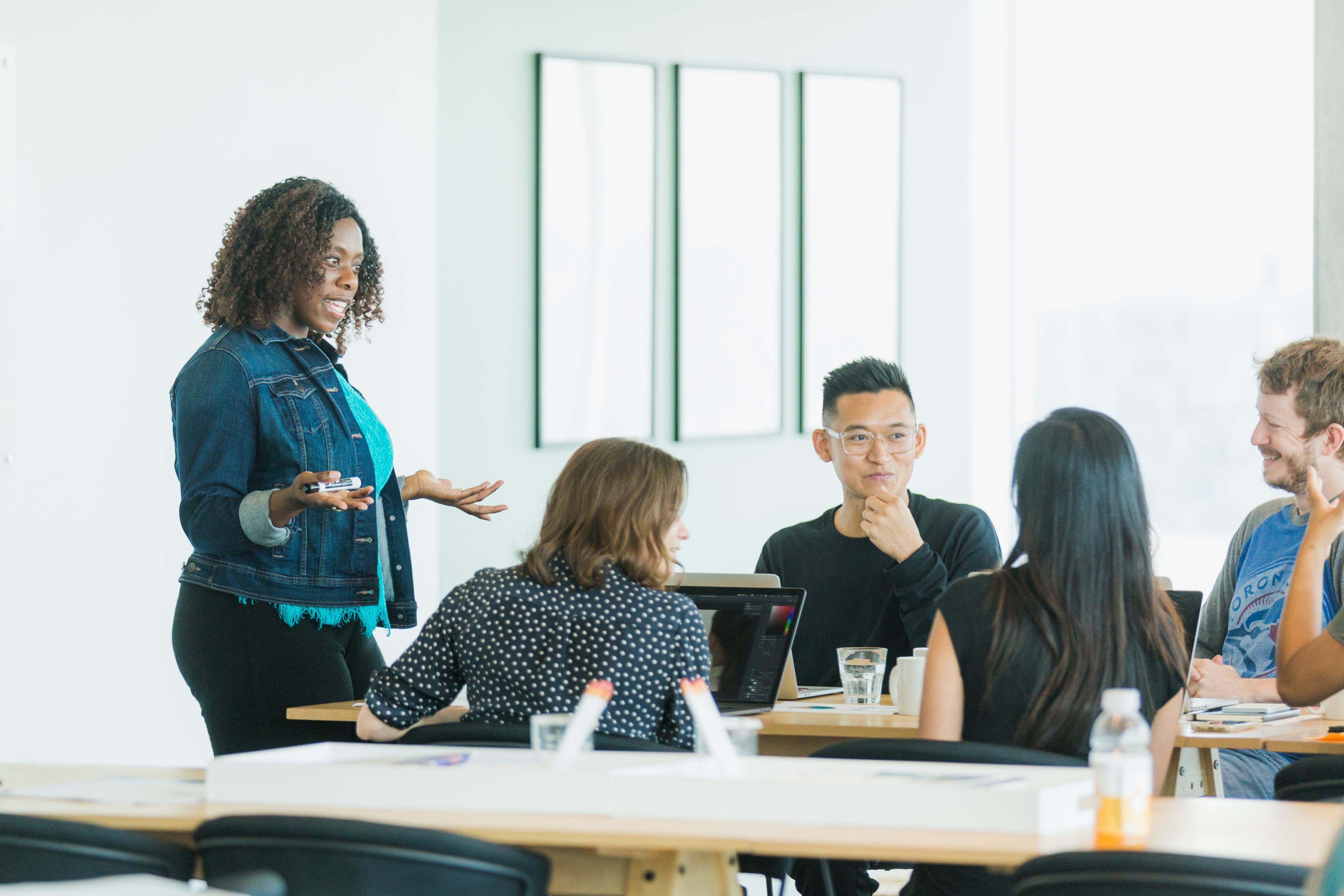 A diverse group of people are gathered around a table in a bright office setting.