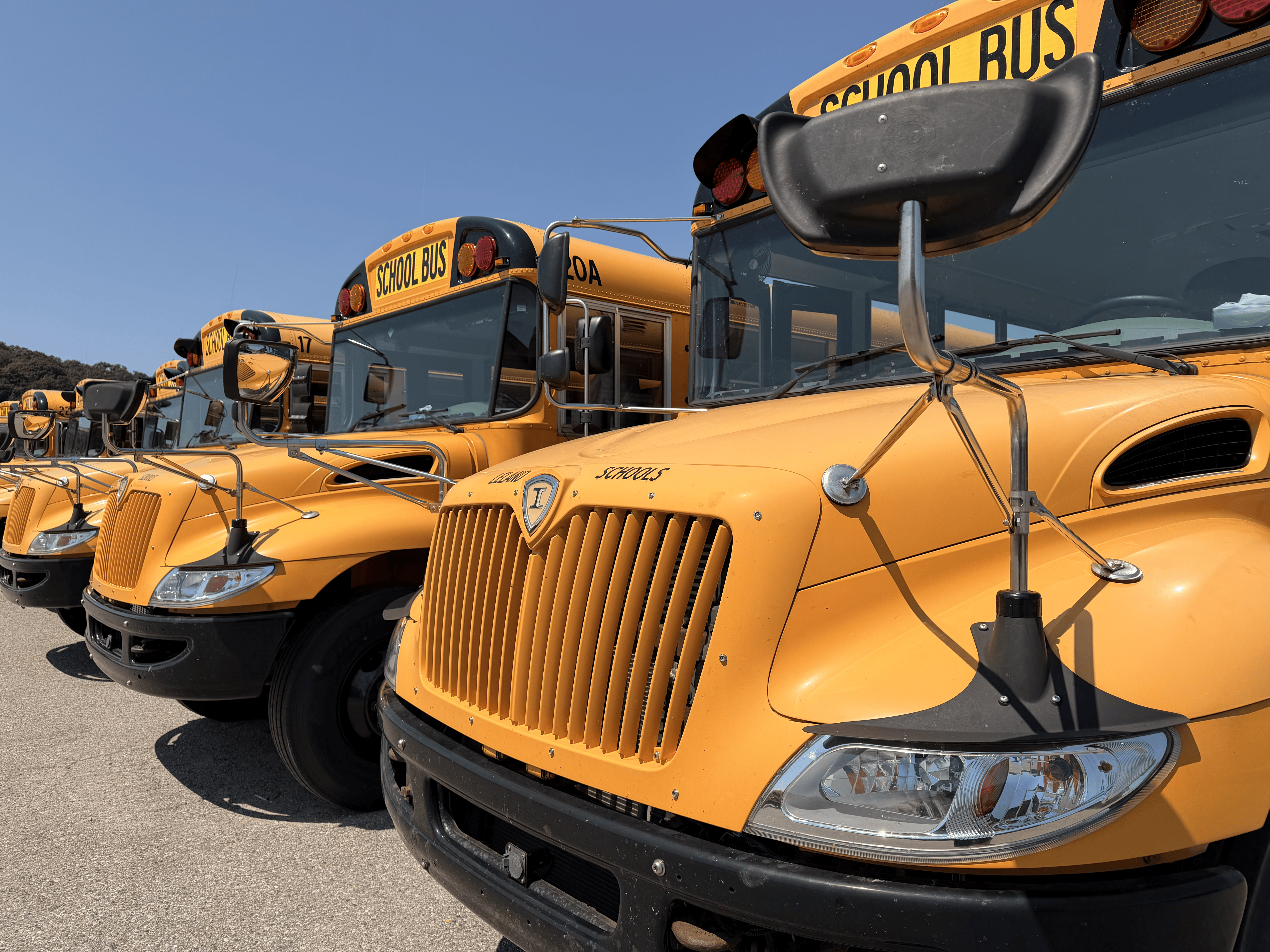 A row of bright yellow school buses parked outdoors under a clear blue sky.