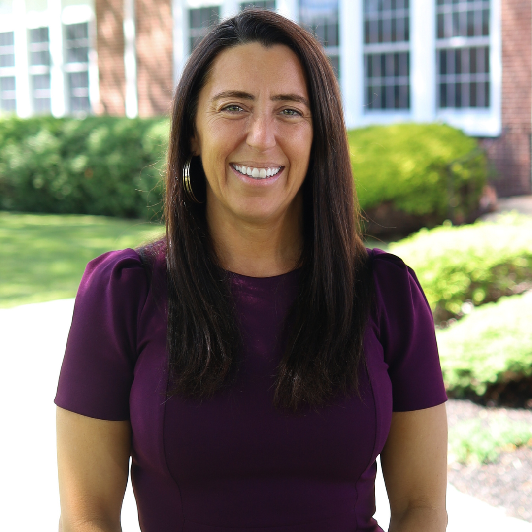 A woman with long, dark hair smiles at the camera, wearing a purple top.