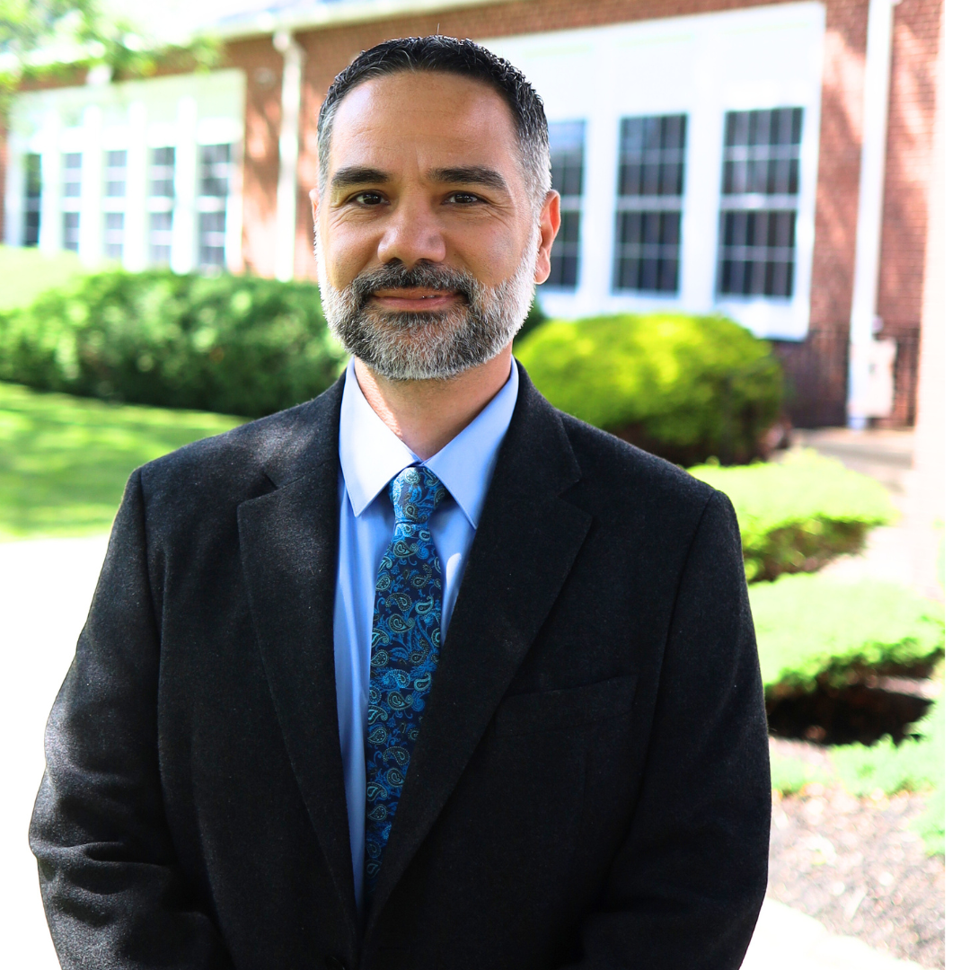 A man in a suit and tie stands outdoors in front of a building.