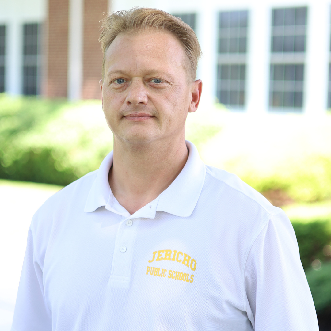 A man wearing a white polo shirt with "Jericho Public Schools" logo stands outdoors.