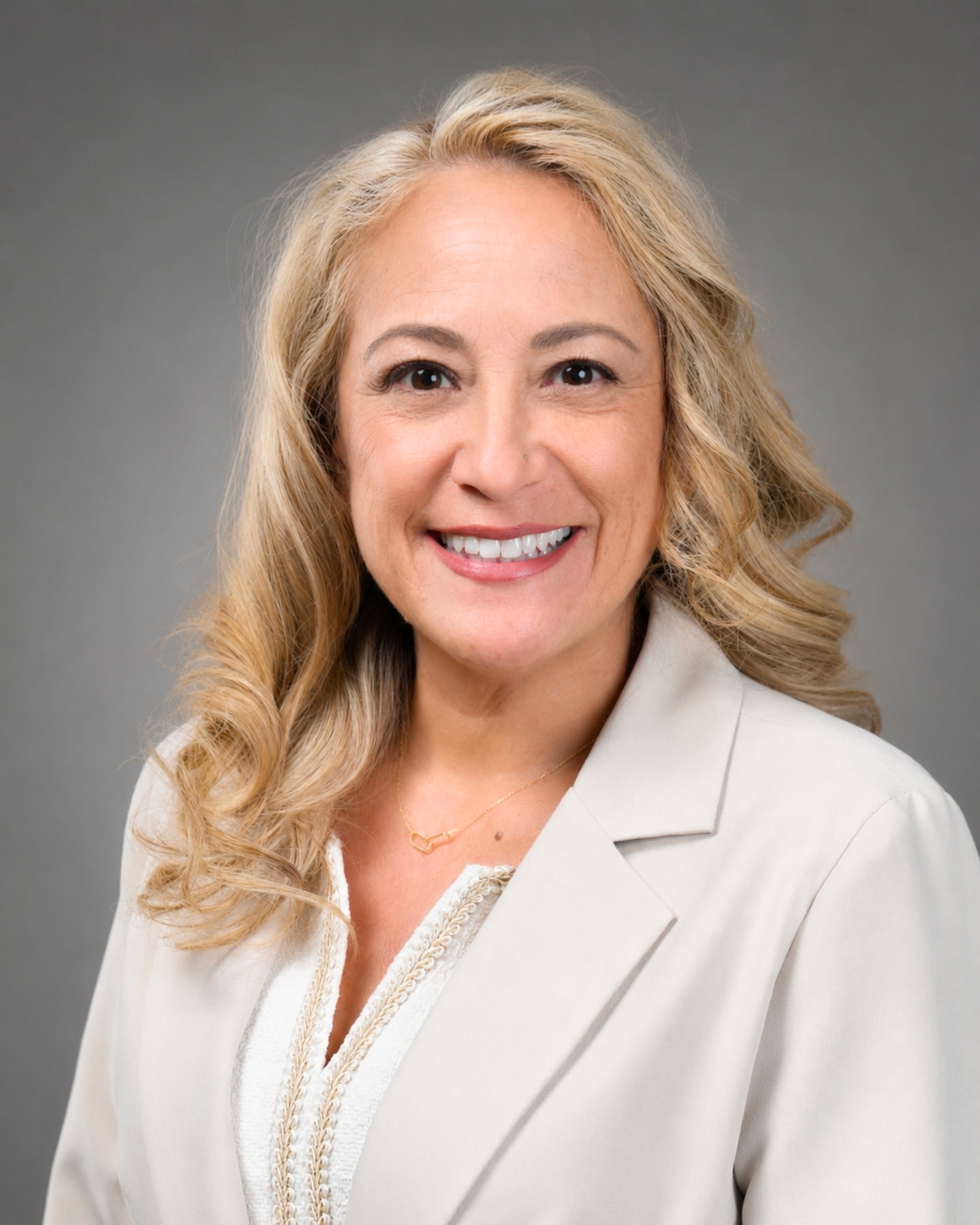 A smiling woman with blonde hair wears a light-colored blazer.