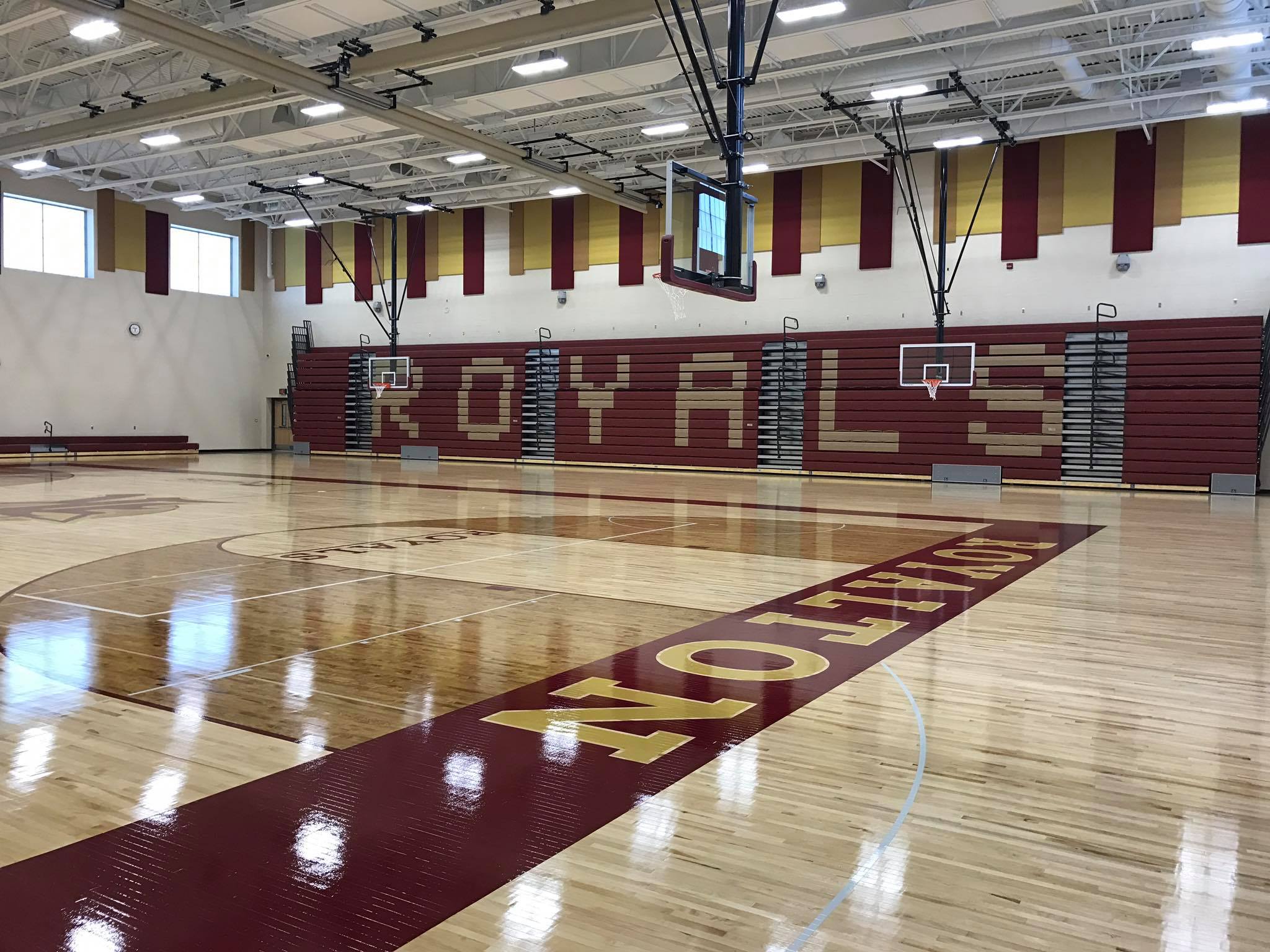 An empty gymnasium with a basketball hoop and the word 'ROYALS' on the wall.