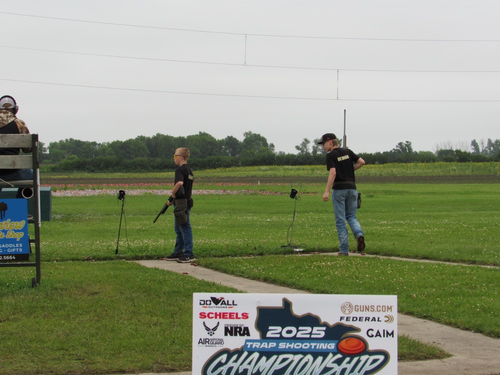 Two people stand on a grassy field, aiming rifles at targets.
