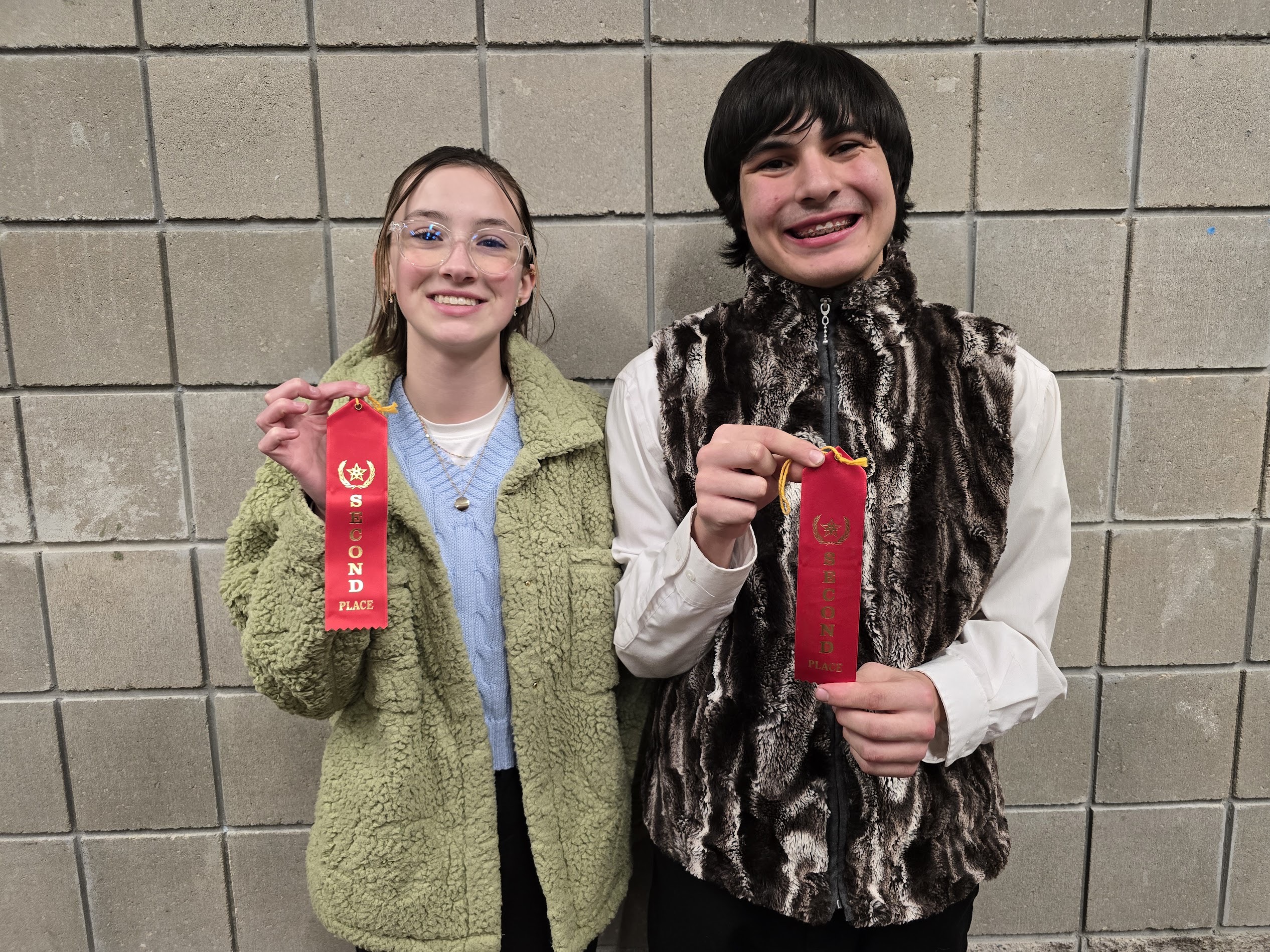 Two smiling people hold up red ribbons in front of a textured wall.