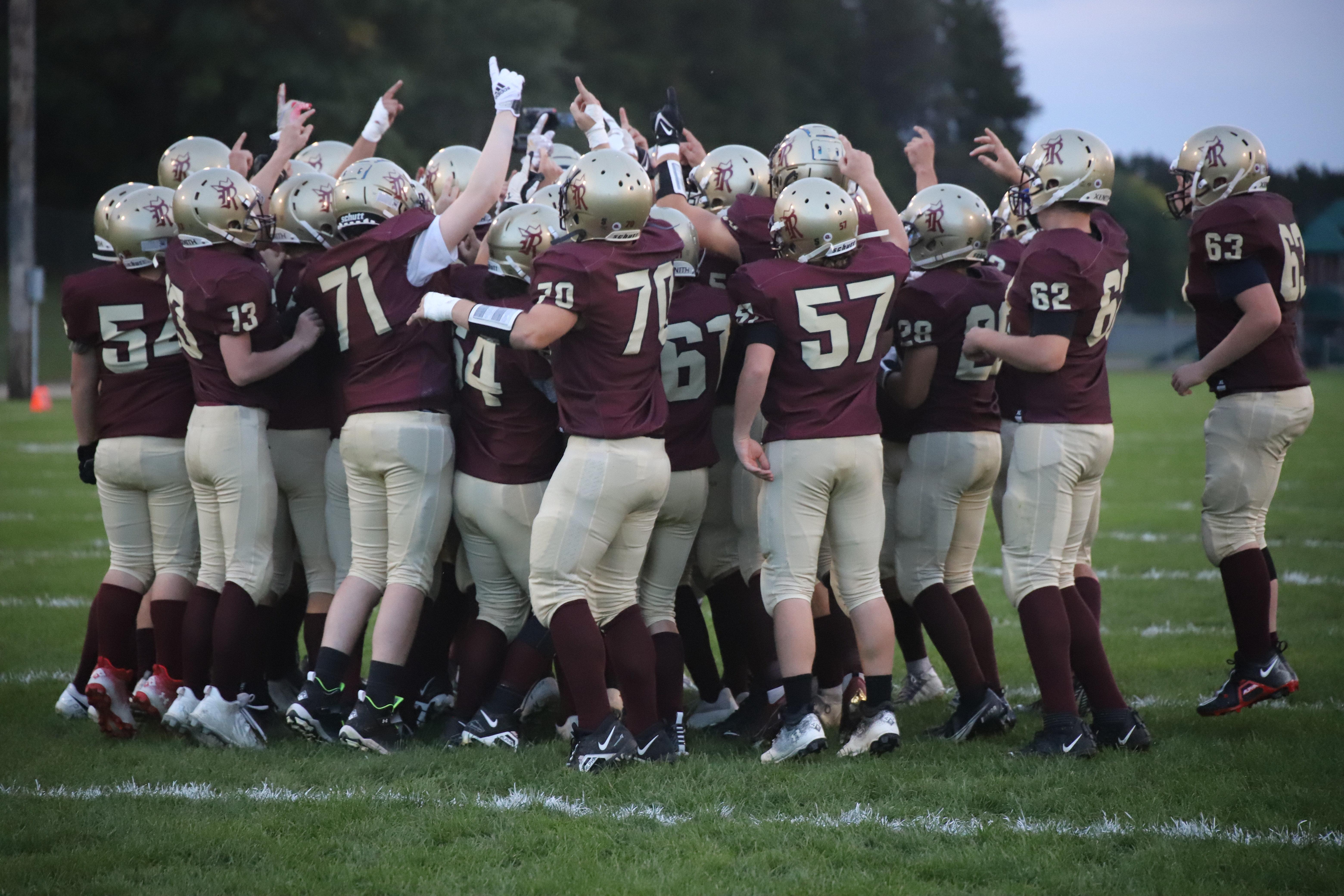 A football team huddles together, celebrating on a green field.