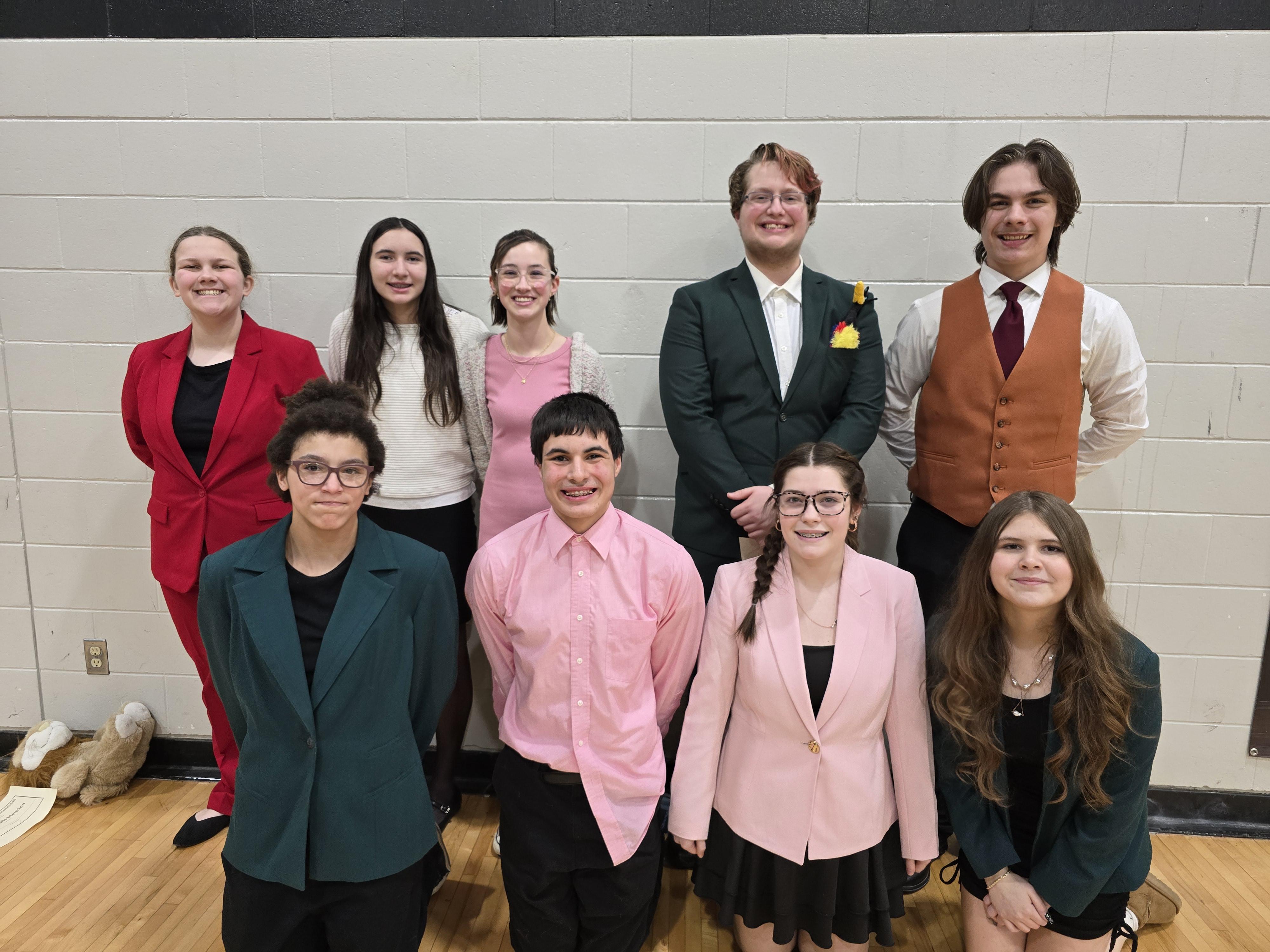 A group of nine people pose for a photo in front of a light-colored wall.