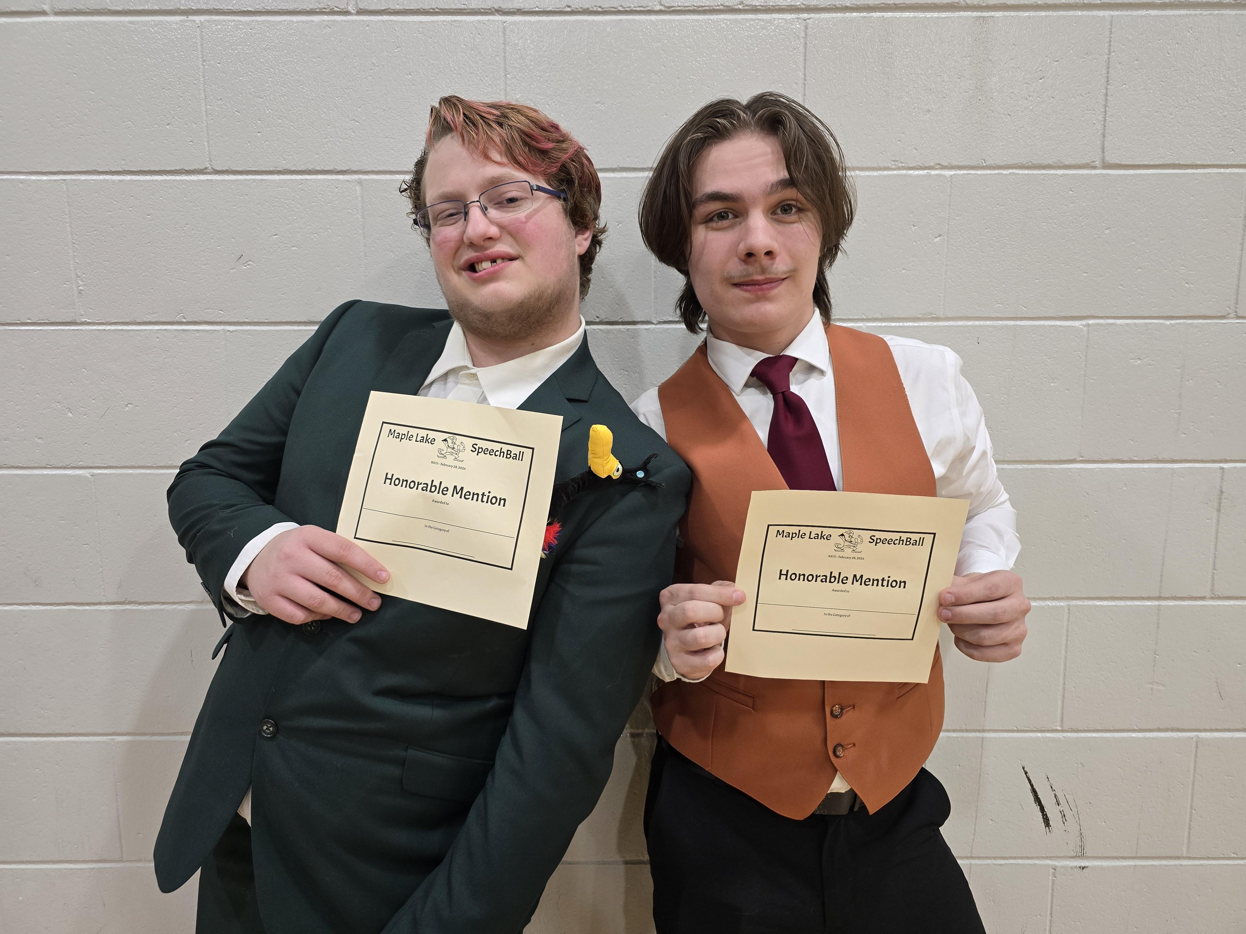Two young men in formal attire pose with certificates, smiling at the camera.