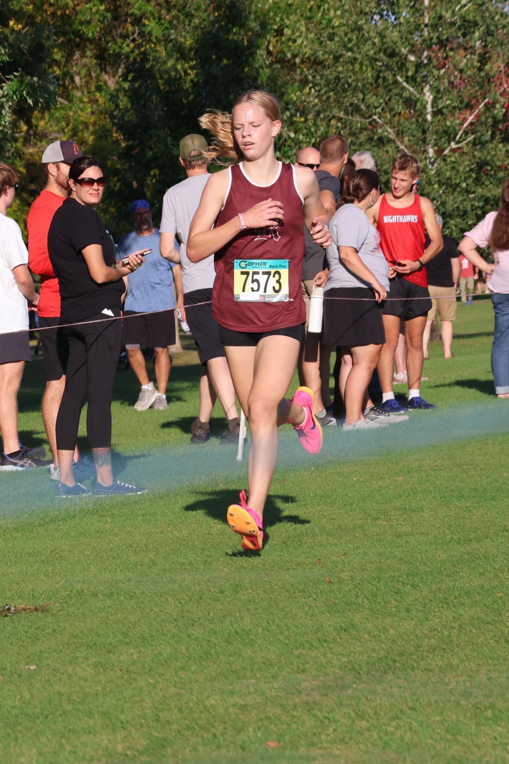 A young woman in a maroon running top races forward on a grassy field.